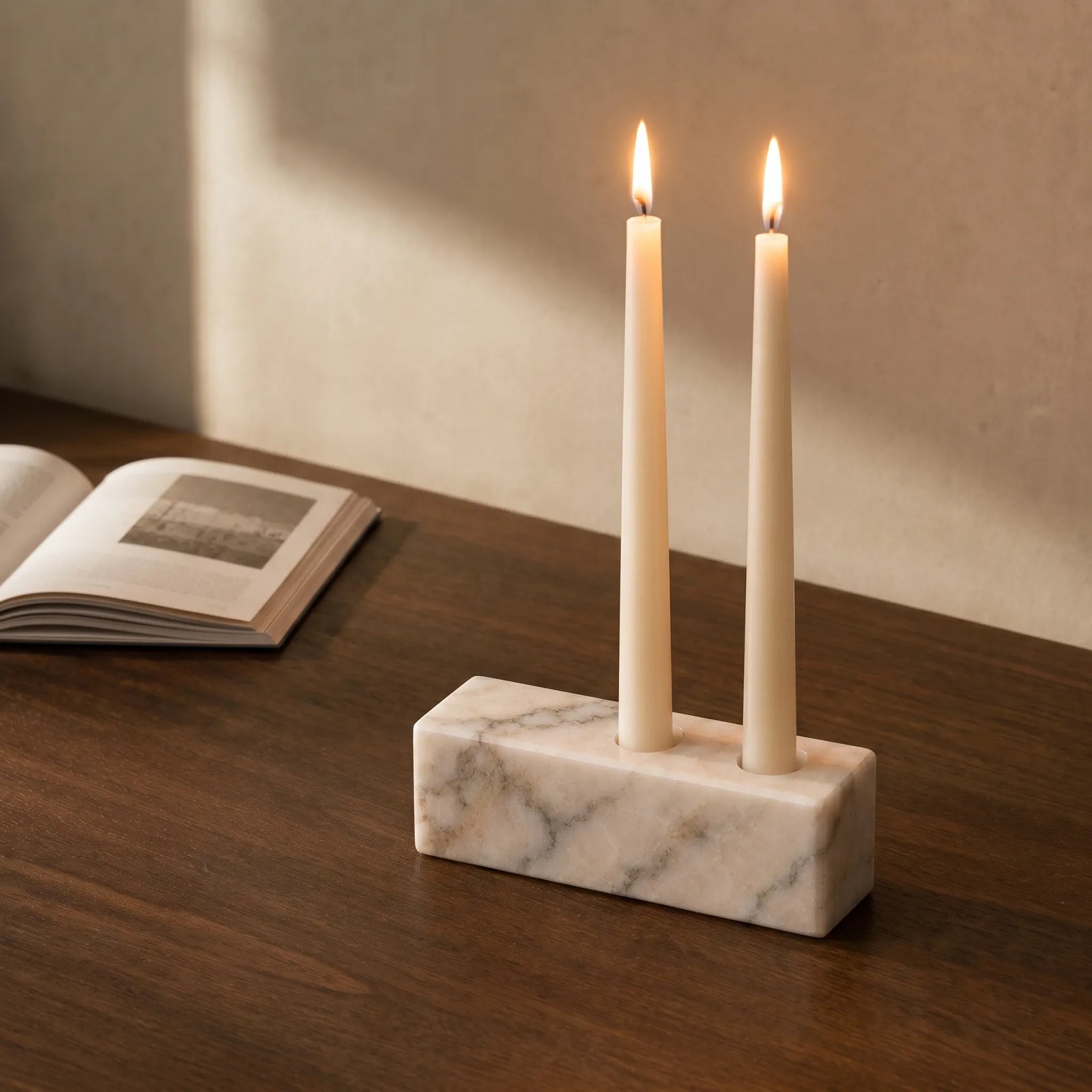 White marble candle holder styled on a walnut desk with an open book.