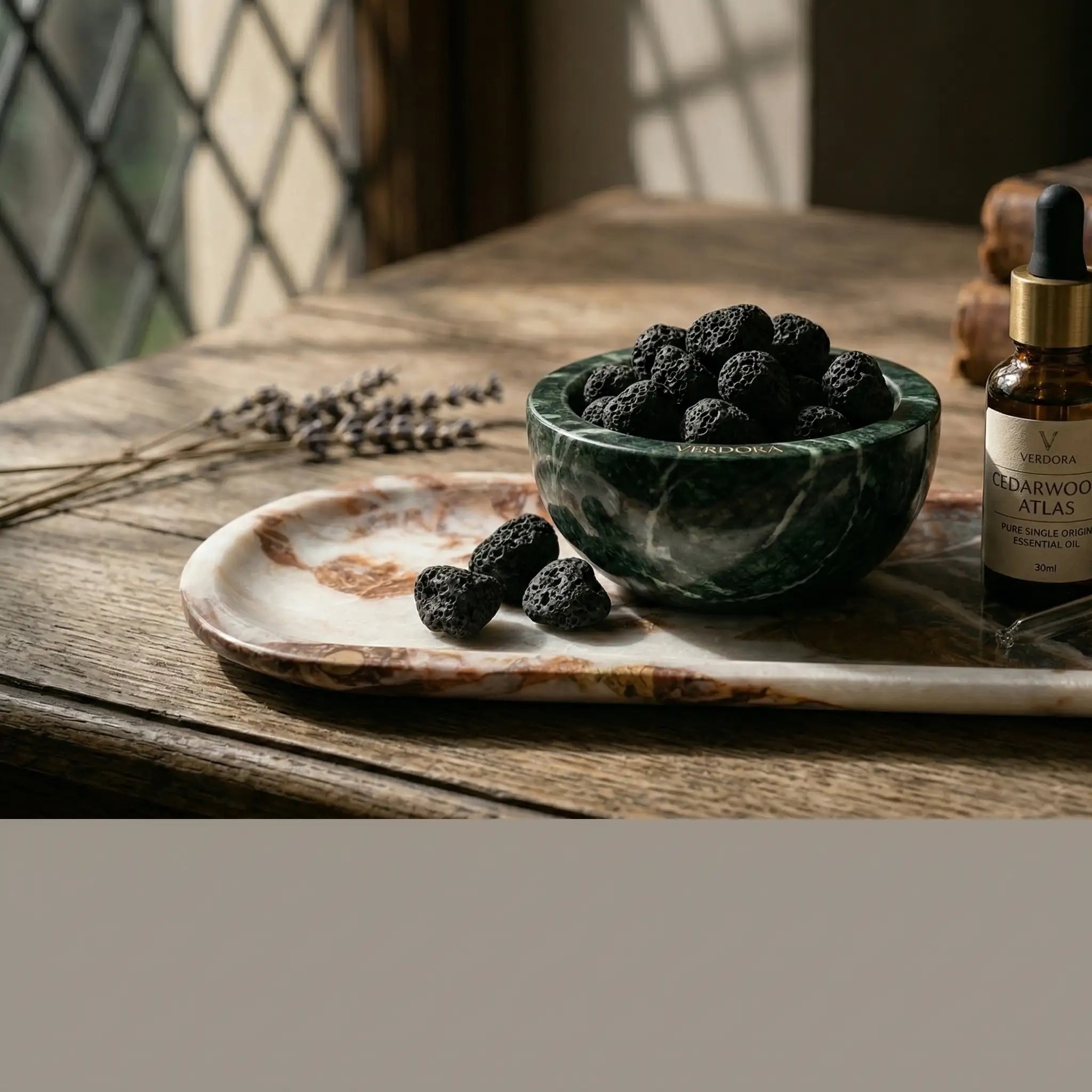 A handcrafted forest green marble bowl filled with black volcanic lava stones used as a natural room fragrance diffuser.