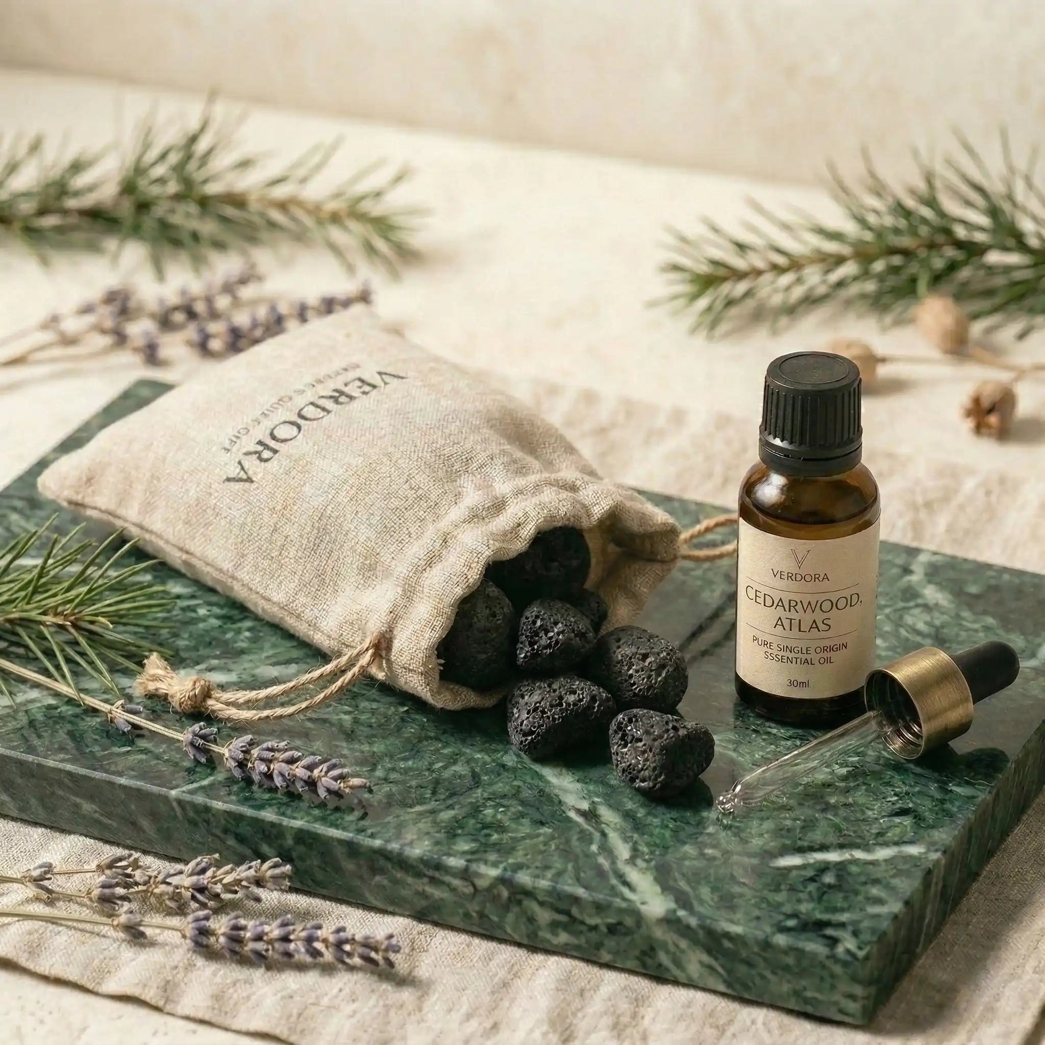 Luxury green marble diffuser tray set with natural lava stones, an essential oil bottle, and a linen pouch on a stone surface.