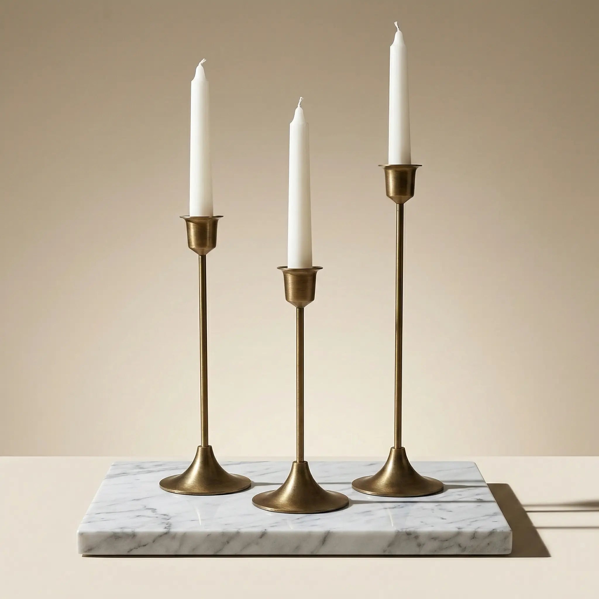 Brass Monolith Trio set of three elegant gold candlestick holders displayed on a white marble base.