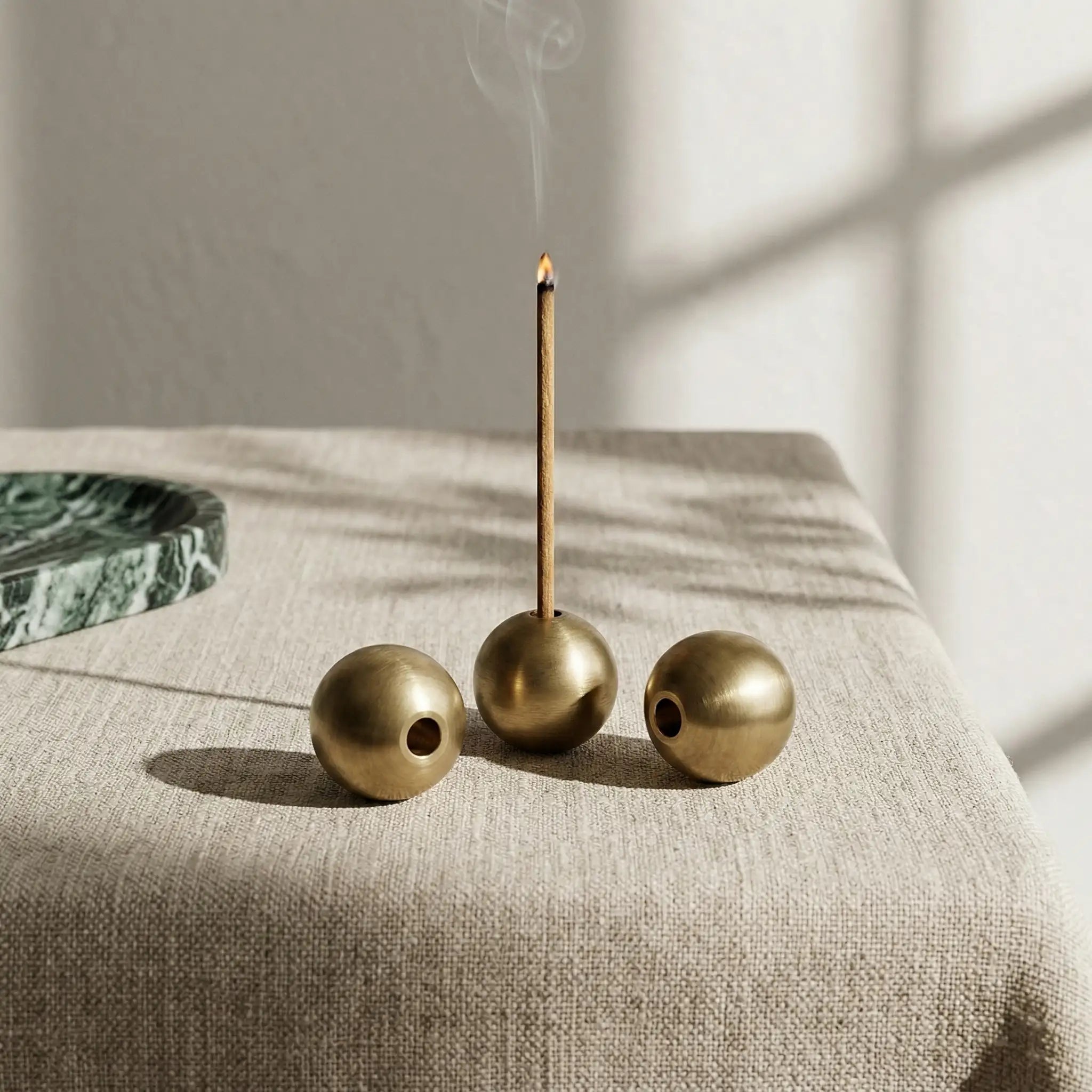 Three Brass Sphere Relics arranged on a linen tablecloth in a bright, sunlit interior setting.