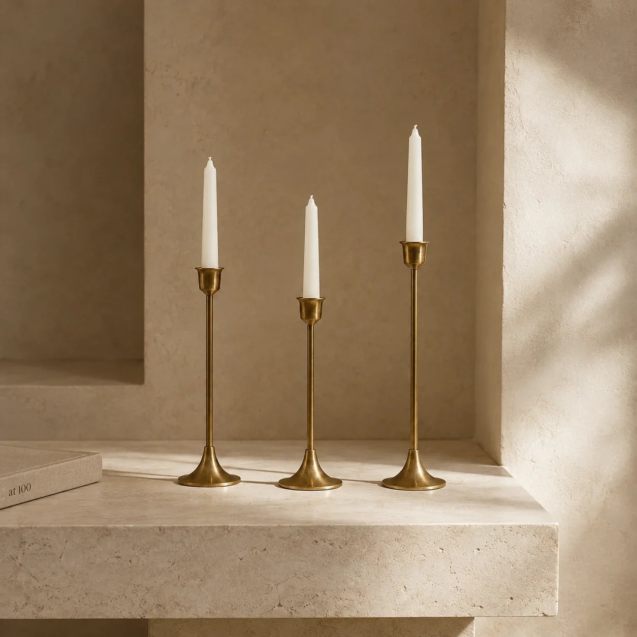 Three brass taper candle holders with white candles on a light stone ledge