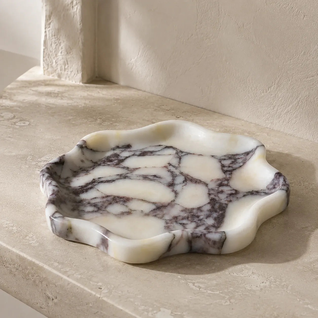 Calacatta Viola marble petal tray with an organic flower-like silhouette, polished edge, shallow carved surface, and unique grey purple natural veining.