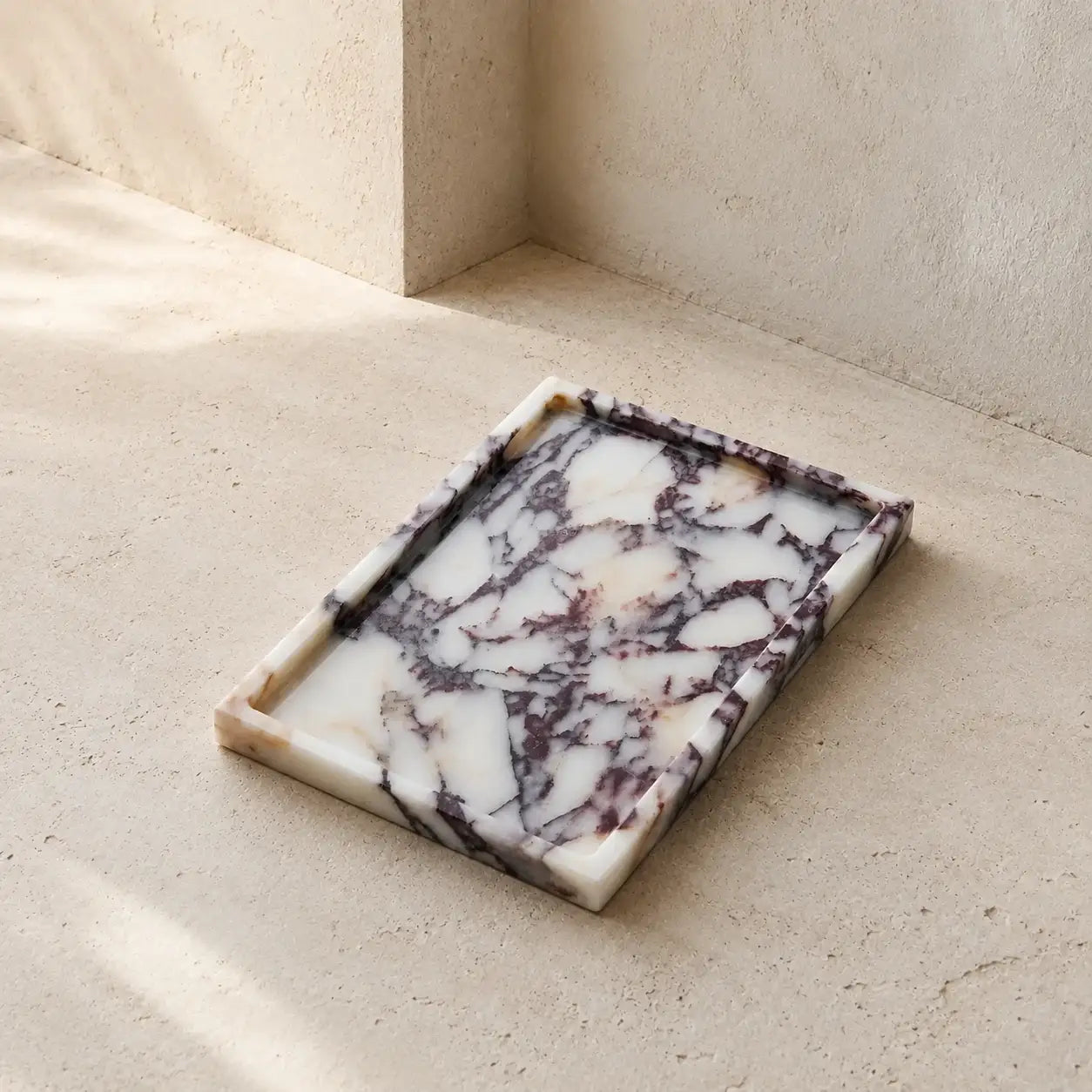 Rectangular Calacatta Viola marble tray with an ivory-white base and natural violet-grey and burgundy veining on a light stone surface.