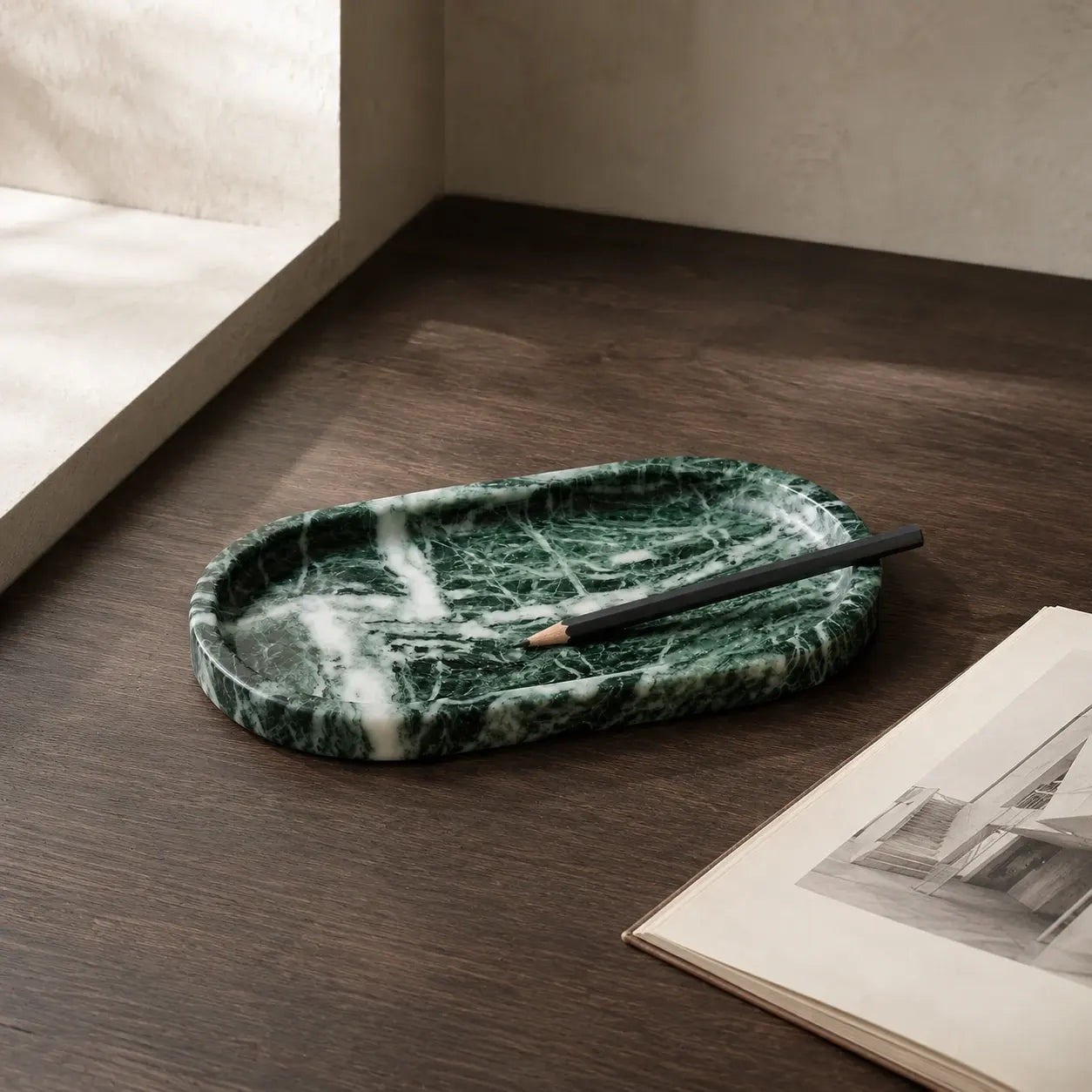 Green marble oval tray with pencil on dark wood desk beside open book