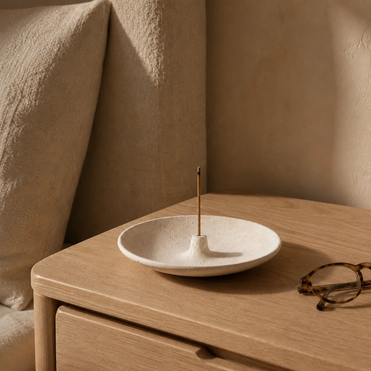 Ivory natural stone incense bowl with incense stick styled on a pale oak bedside table in a warm reading corner