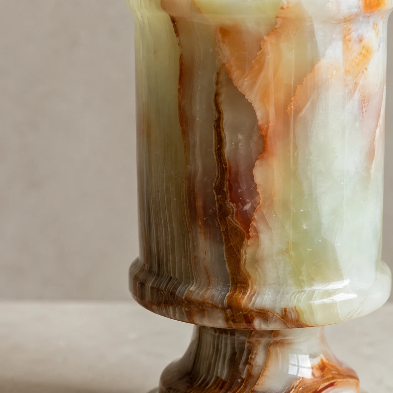 Close-up detail of a natural onyx candle holder showing layered mineral patterns, green and amber stone tones, polished surface, and unique geological variations.