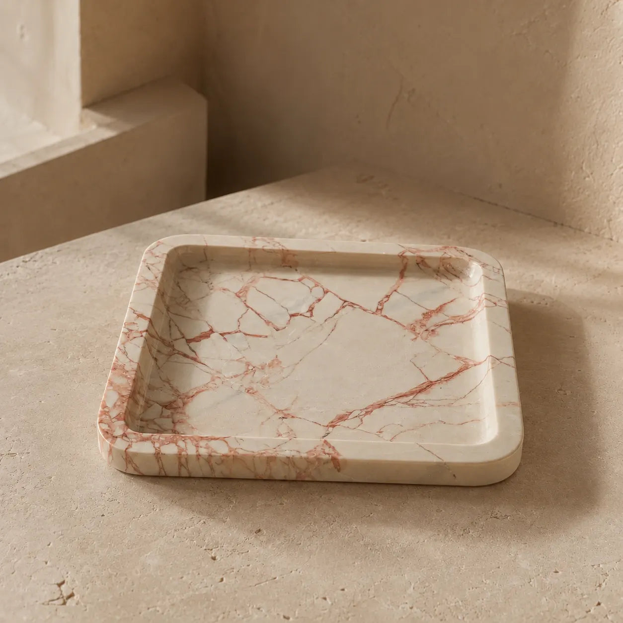 Pink veined natural marble tray with a rounded rectangular silhouette, shallow carved surface, polished edge, and unique rose-colored mineral veining on warm white stone.
