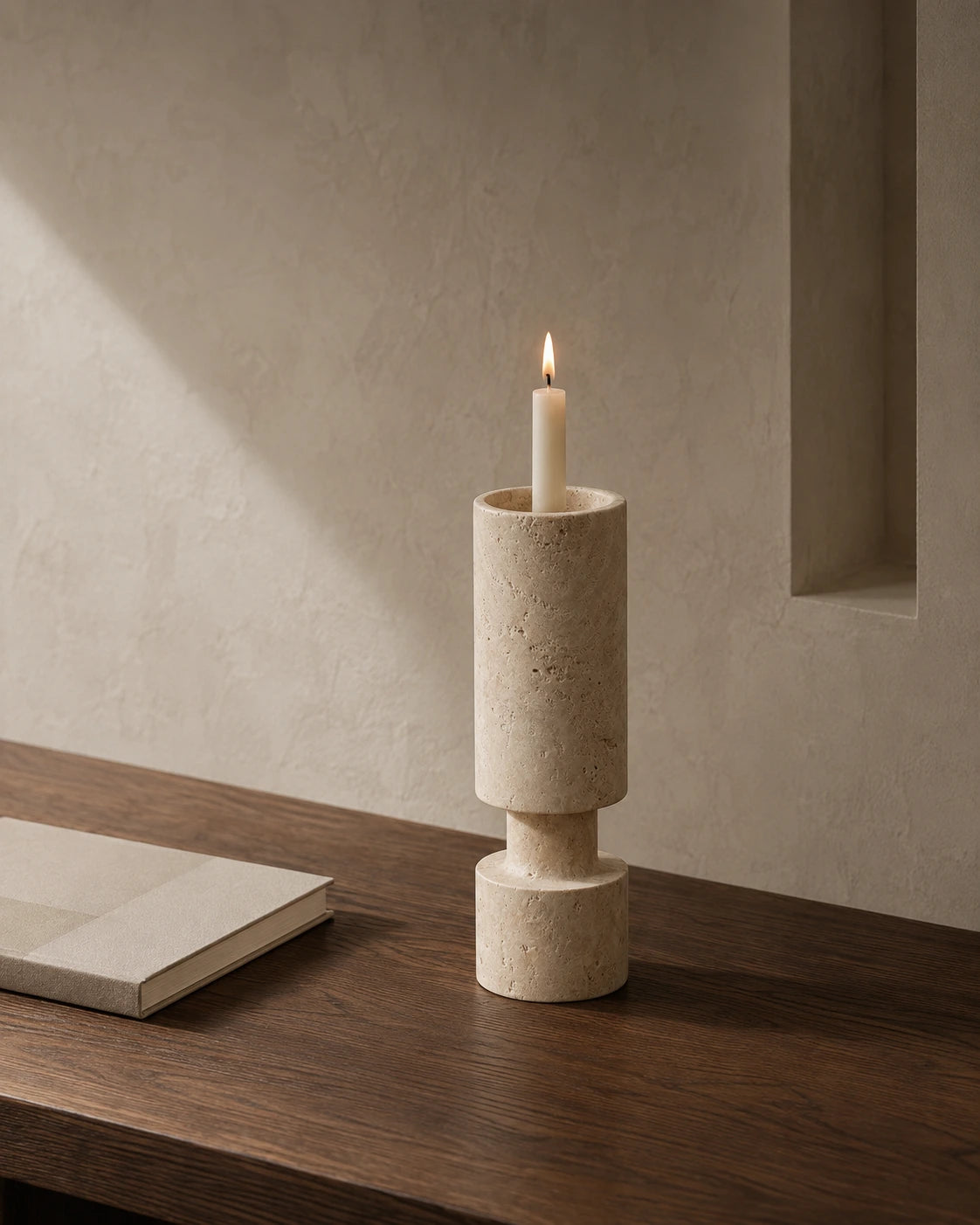 Travertine cylinder candle holder with ivory taper candle on a dark wood table
