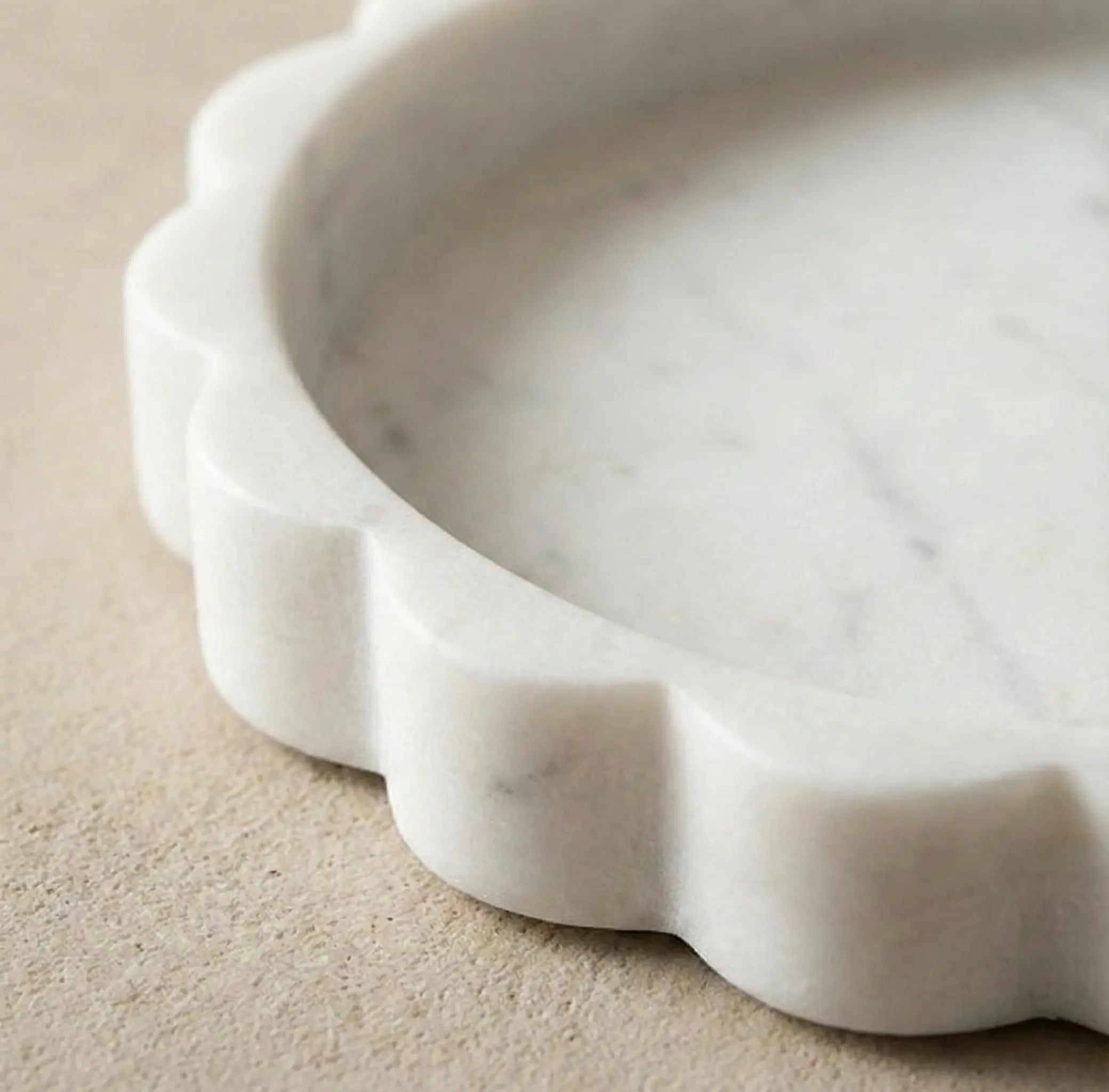 Close-up detail of the hand-carved sawtooth scalloped edge on a premium white marble circular tray.