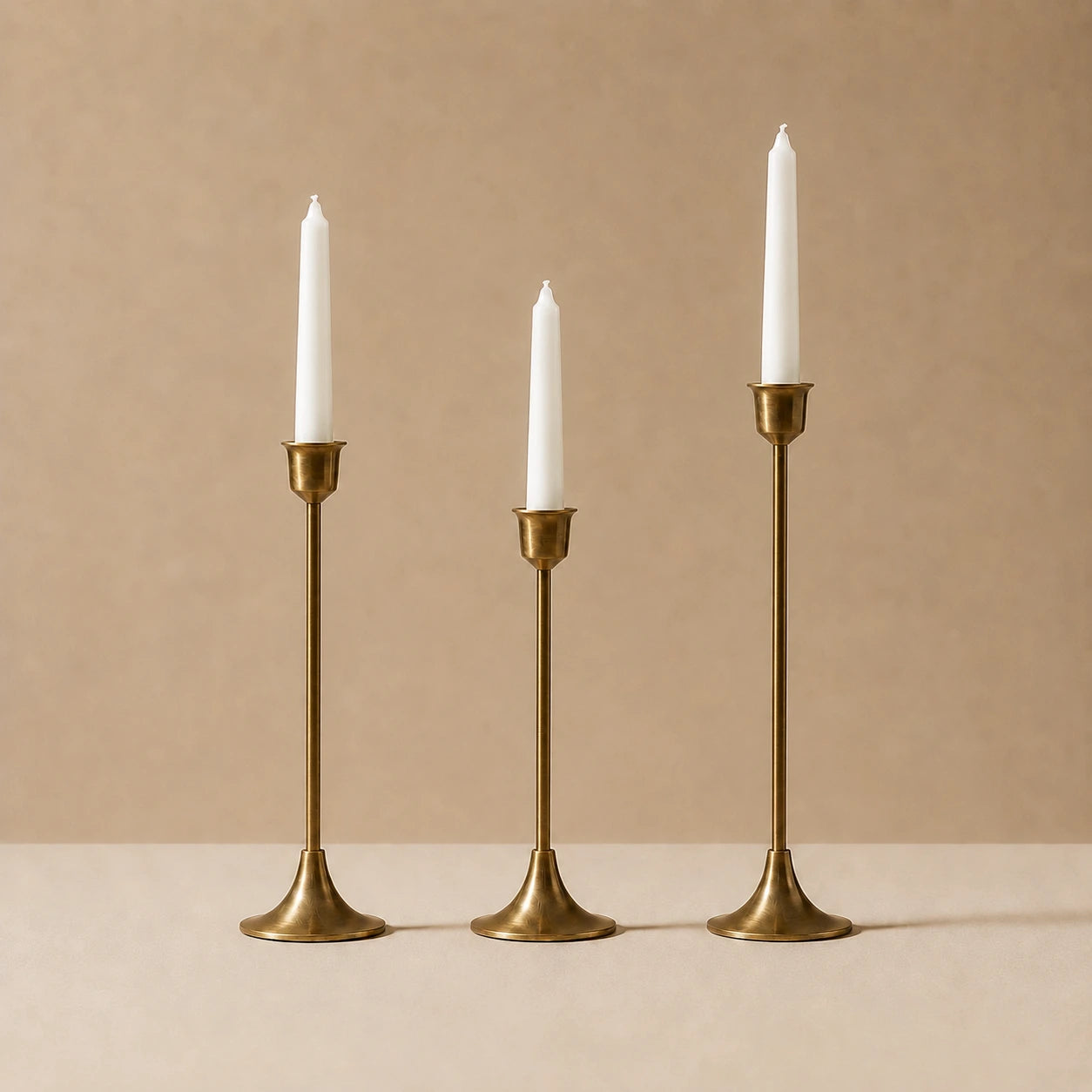 Set of three solid brass candlestick holders in small, medium, and large sizes with slim ivory taper candles, showing their graduated heights and warm satin brass finish.