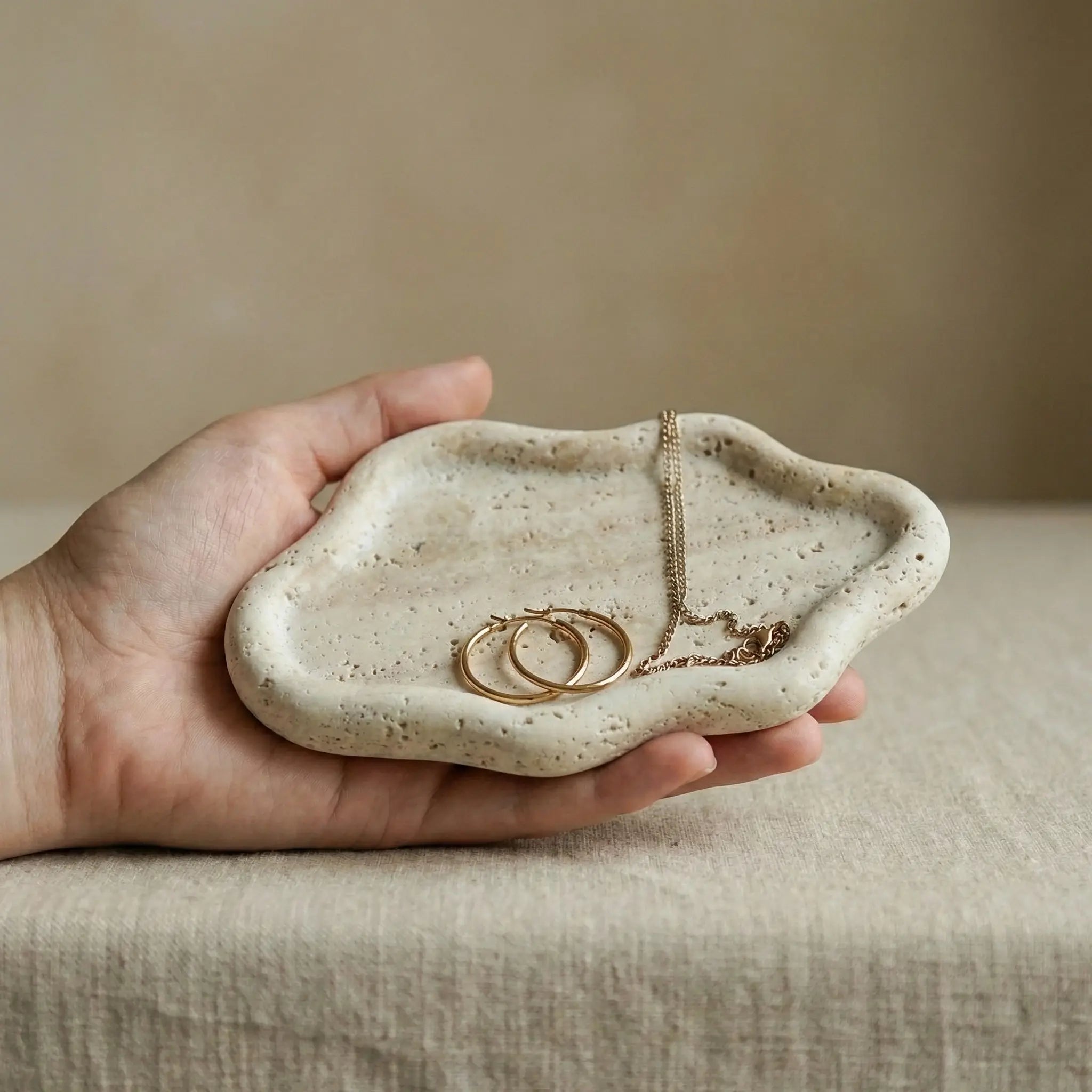 Hand holding Travertine Cloud Tray with jewelry to show compact size and handcrafted detail