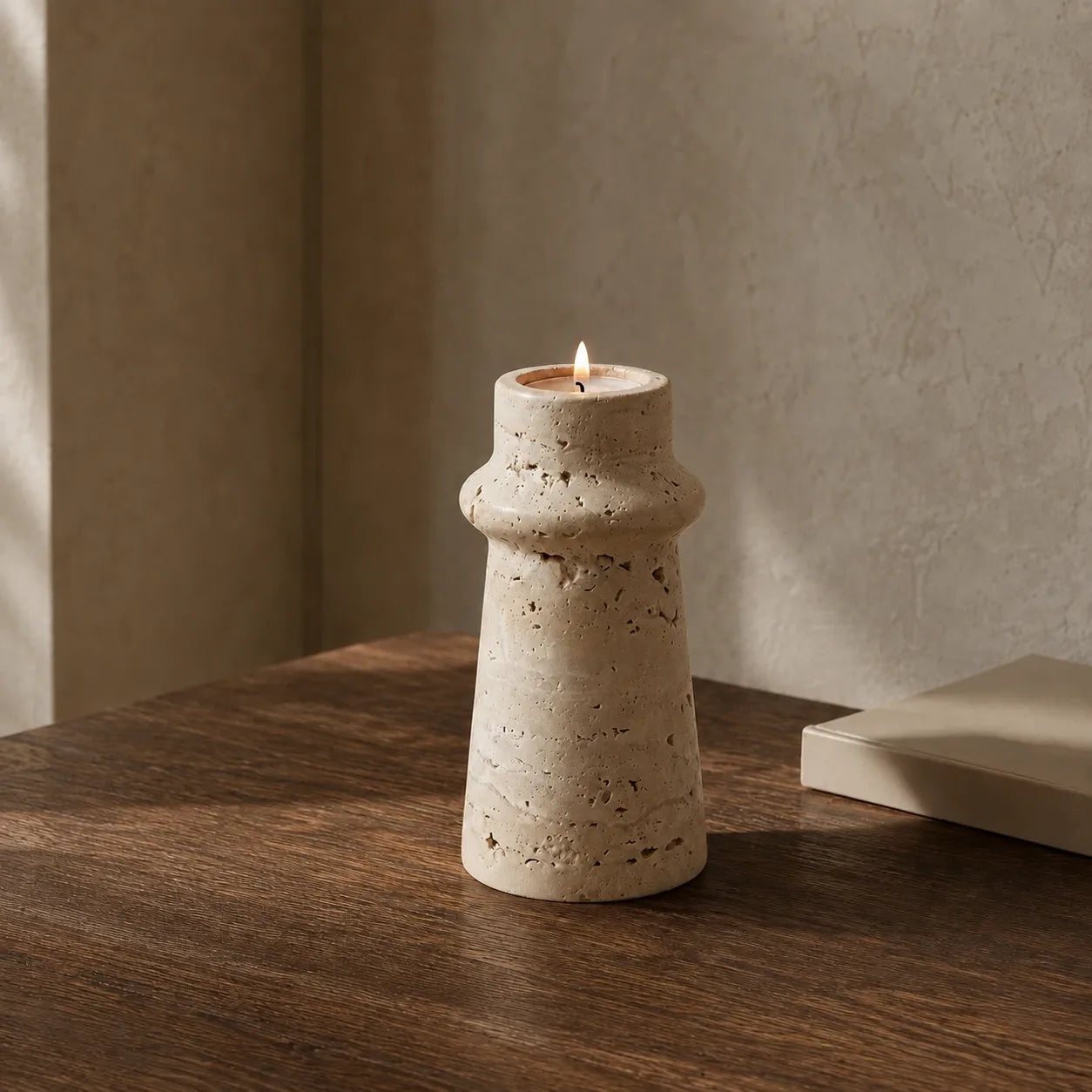 Travertine collar candle holder with lit candle on a dark wood table