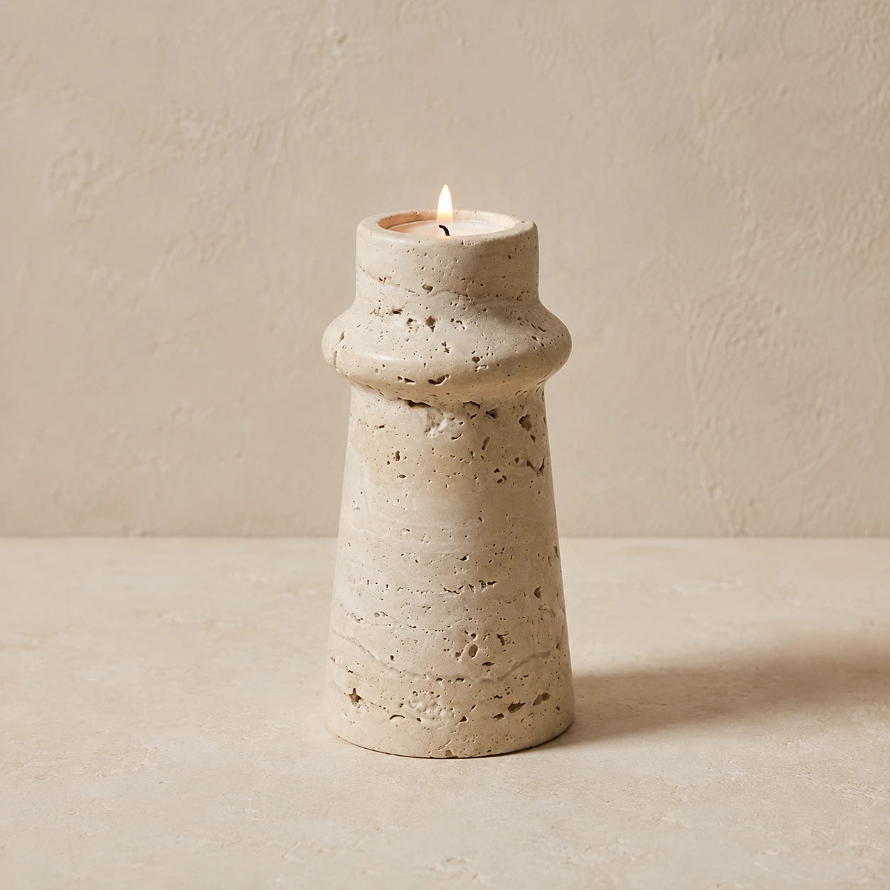 Sculptural travertine candle holder with rounded collar detail and lit candle
