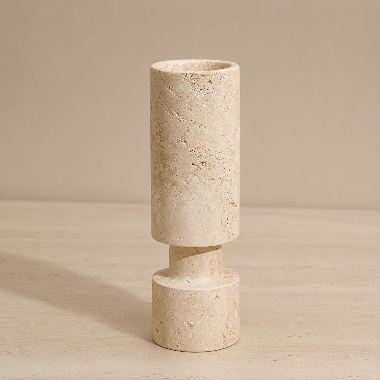 Sculptural travertine candle holder with cylindrical form on a warm neutral background