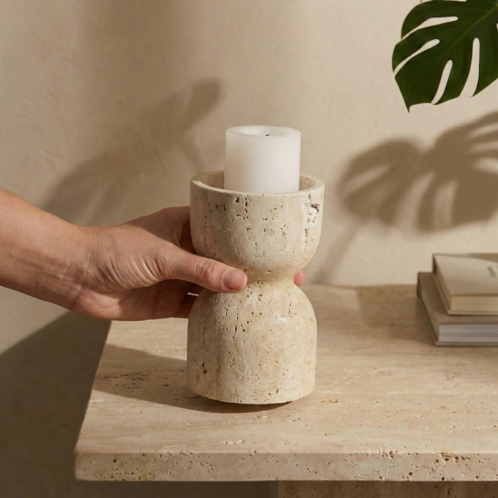 Hand placing a pillar candle into the Travertine Hourglass Holder on a minimalist stone tabletop.