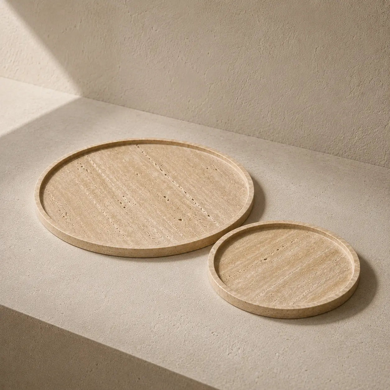 Small 20 cm and large 30 cm round travertine trays shown together in a warm minimal interior.