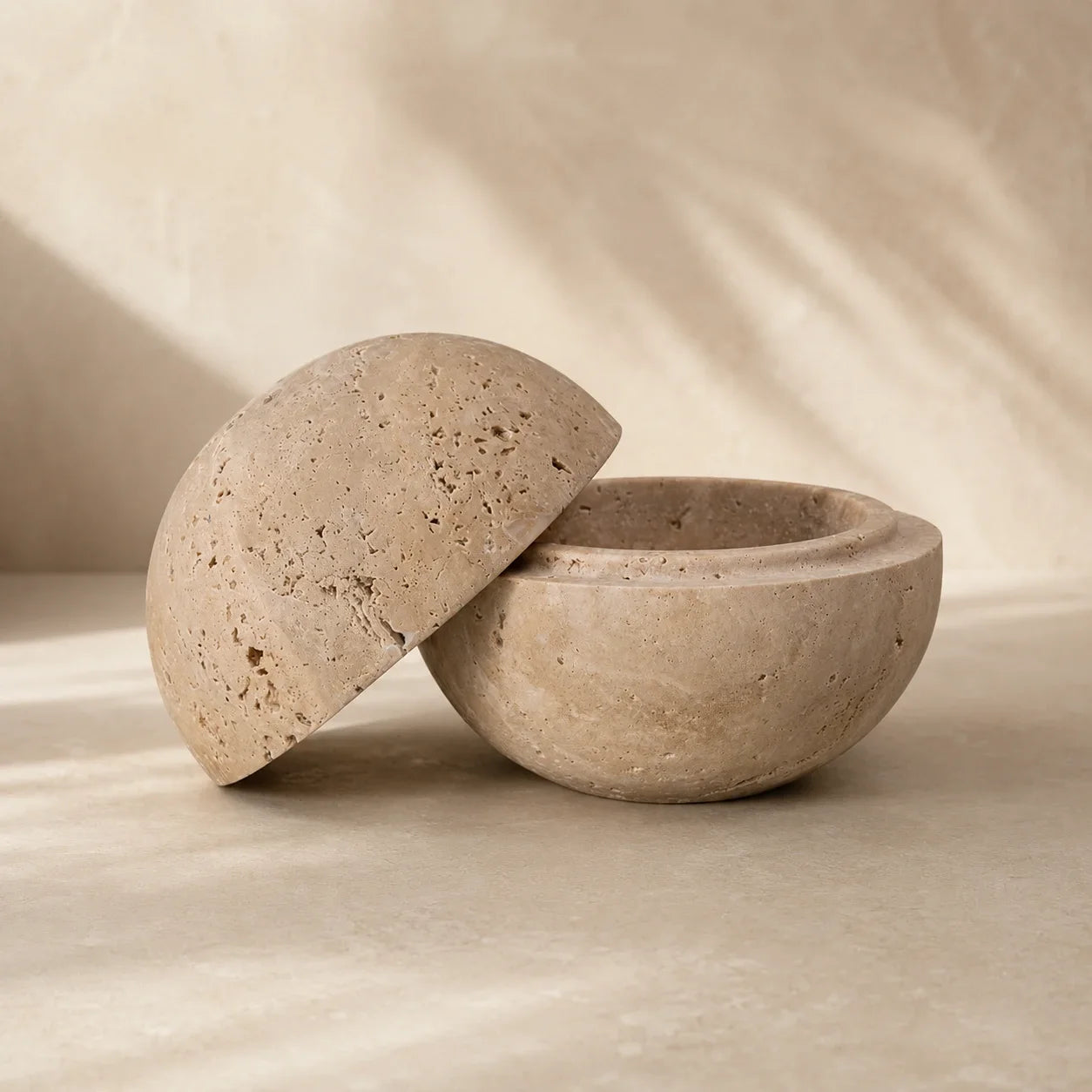 Travertine stone bowl with a dome lid styled against a warm neutral plaster background