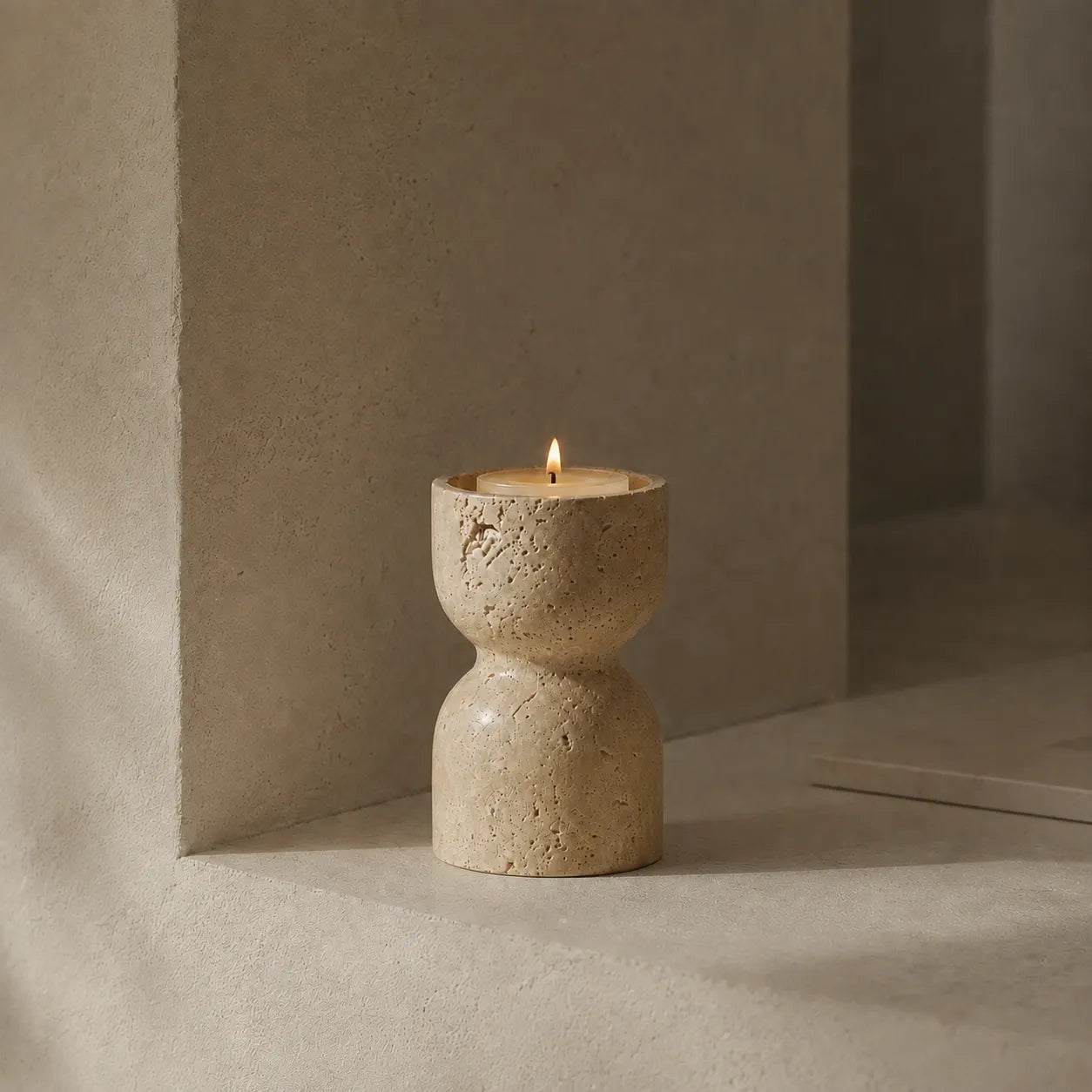 Travertine hourglass candle holder with a short ivory candle in a quiet architectural stone niche