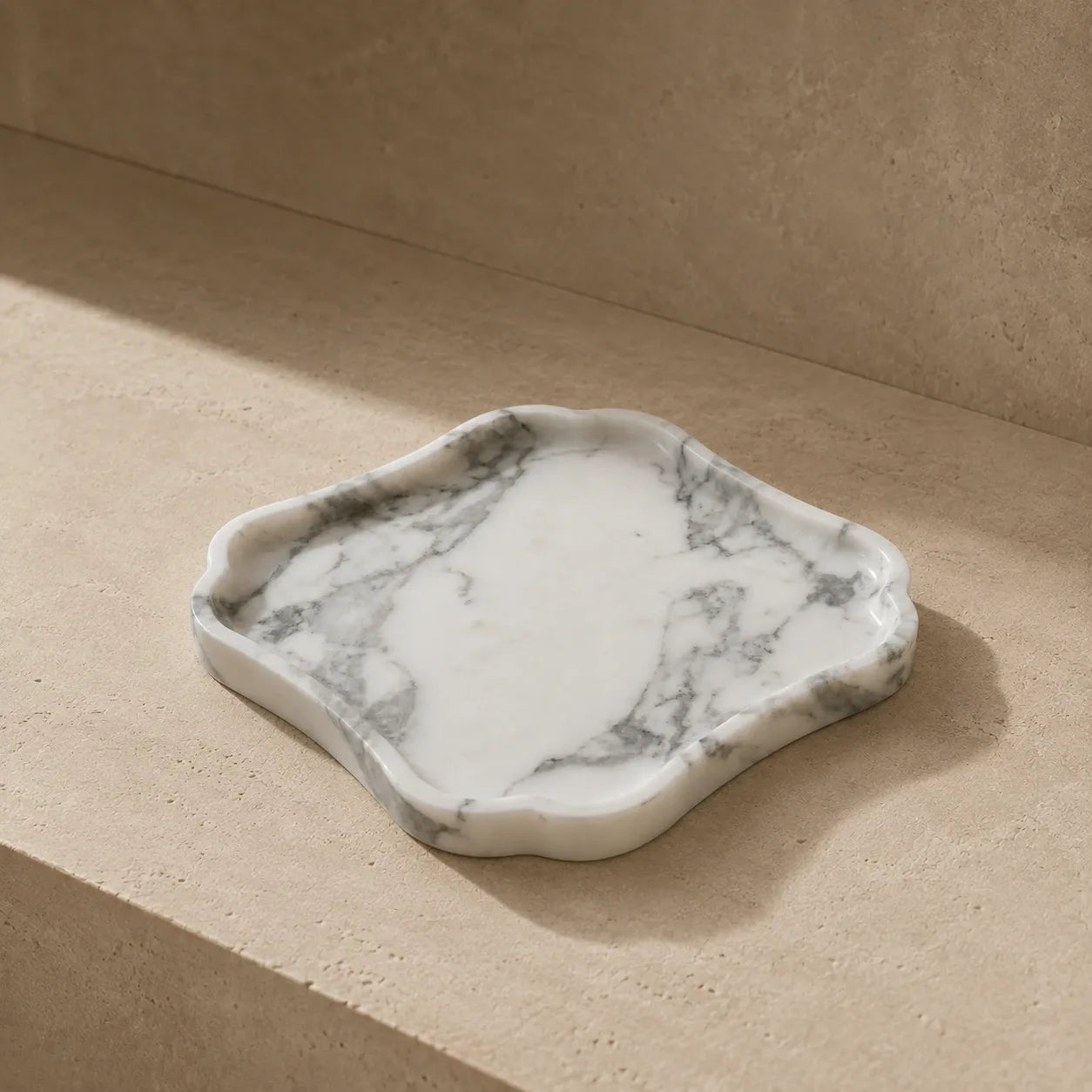 White and grey veined natural marble tray with an organic geometric shape on a limestone surface, showcasing its polished stone edge, shallow carved design, and unique marble variation.