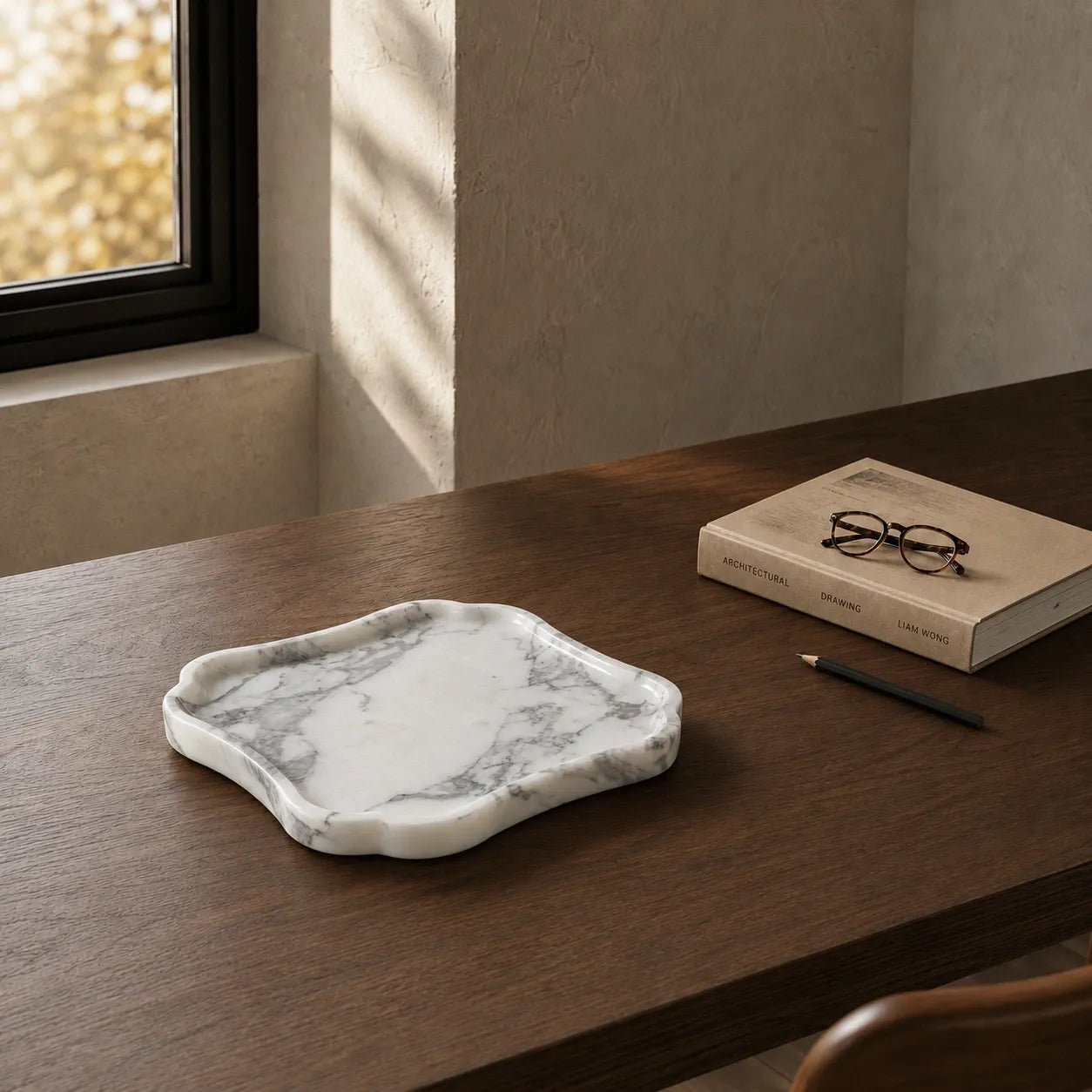 White and grey veined natural marble tray on a walnut desk with an architecture book, reading glasses, and pencil, showcasing its organic shape, polished stone edge, and refined marble surface.