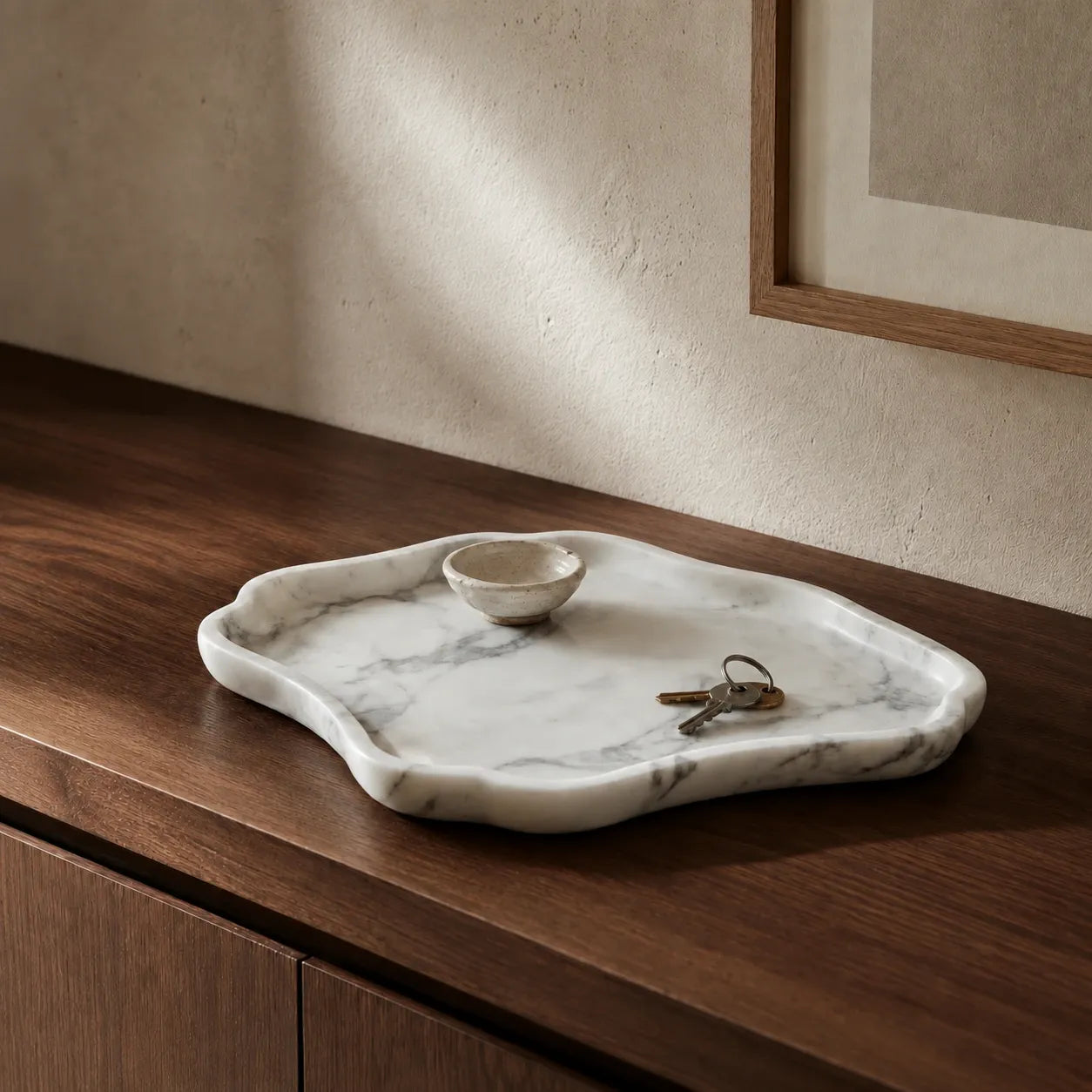 White and grey veined natural marble tray styled on a walnut entryway console with a ceramic bowl and keys, highlighting its organic shape, polished stone edge, and timeless marble surface.