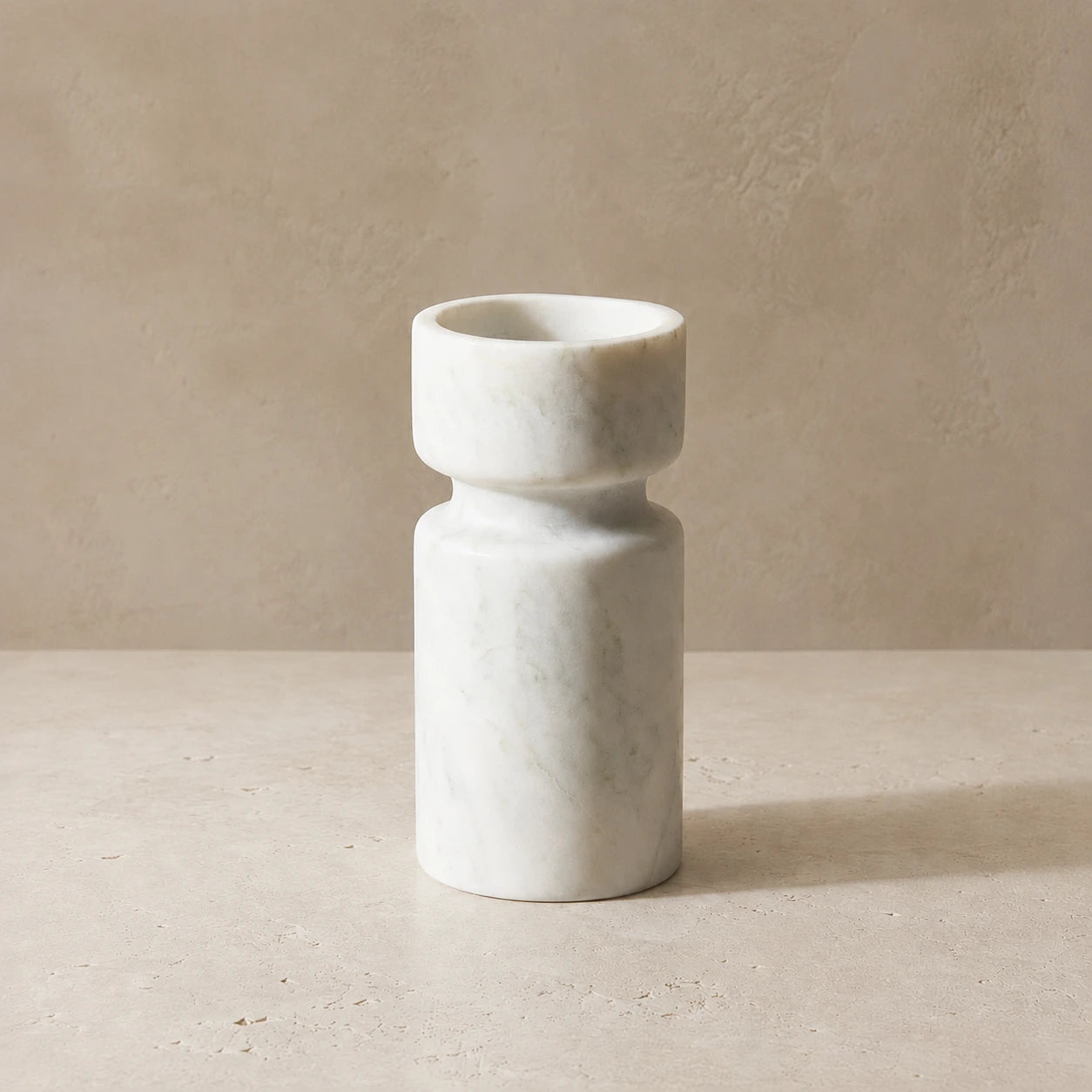 White marble sculptural candle holder on a warm neutral stone surface