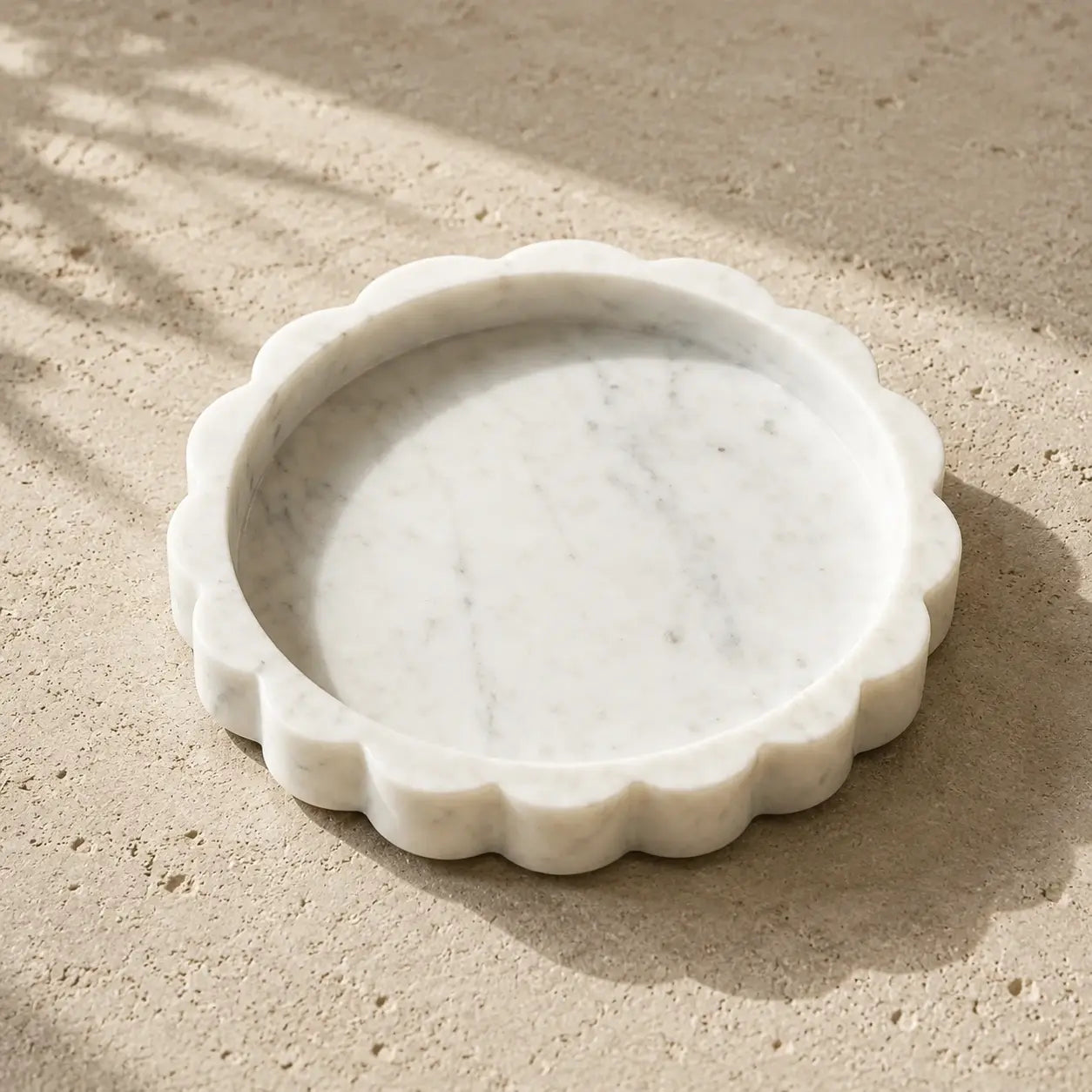 White natural marble scalloped tray with an organic flower-like shape on a limestone surface, showcasing its rounded carved edge, shallow design, polished stone finish, and subtle natural marble variation.