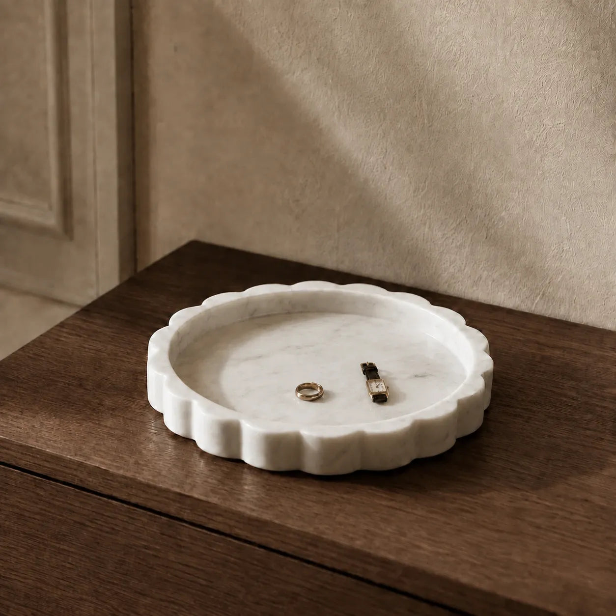 White scalloped marble tray on a walnut dresser with a watch and ring, showing its sculptural edge, natural stone texture, and compact scale.