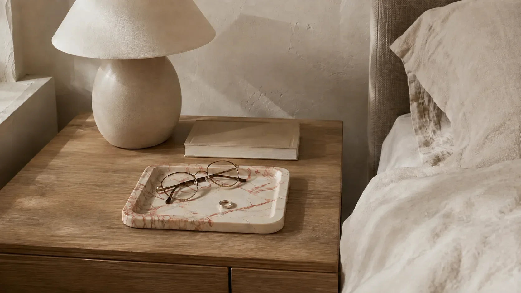 Bedroom bedside table with a rose-veined marble tray, glasses, linen bedding and a sculptural lamp