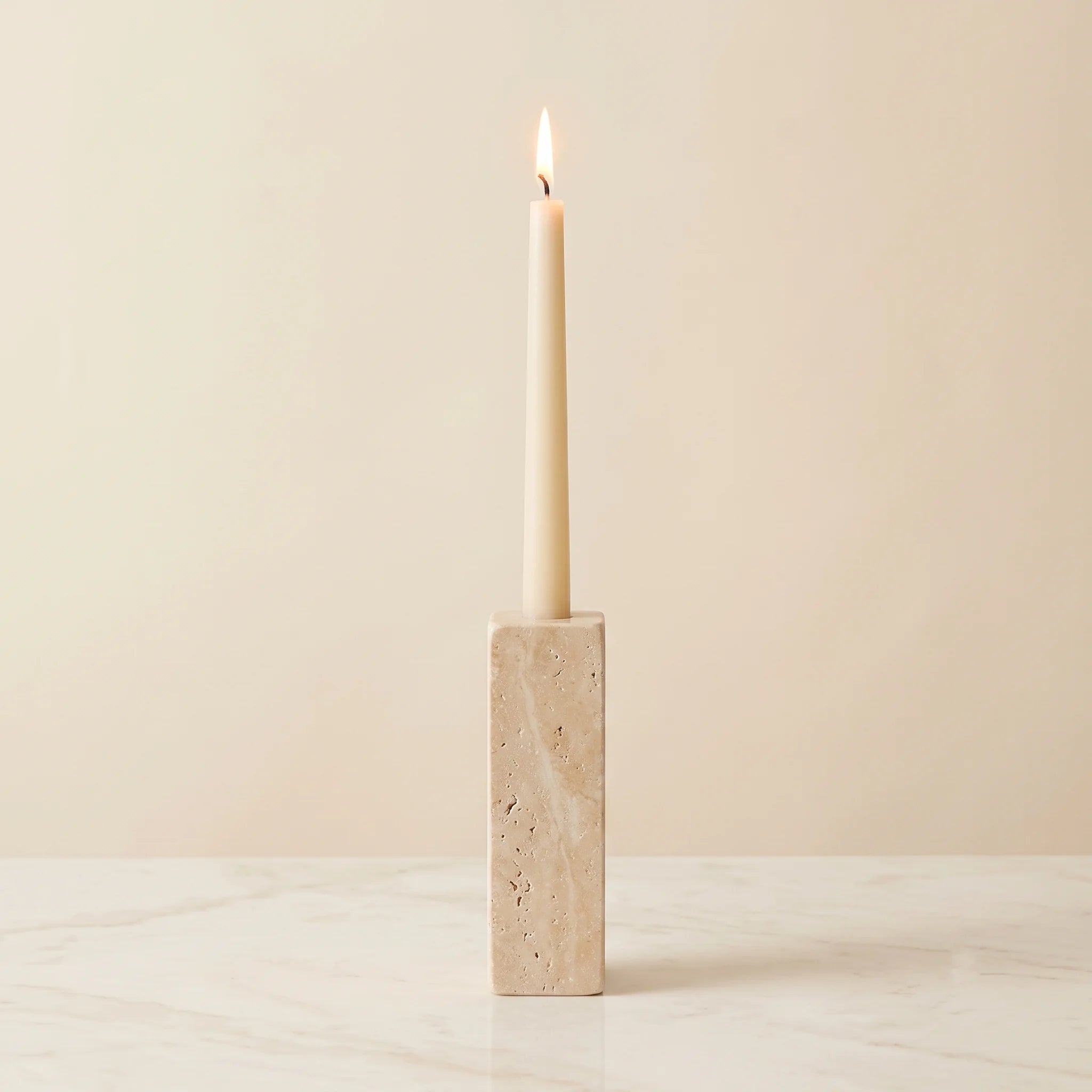 Monolith Candle Holder in Travertine — warm fossil-textured natural stone with a lit taper candle