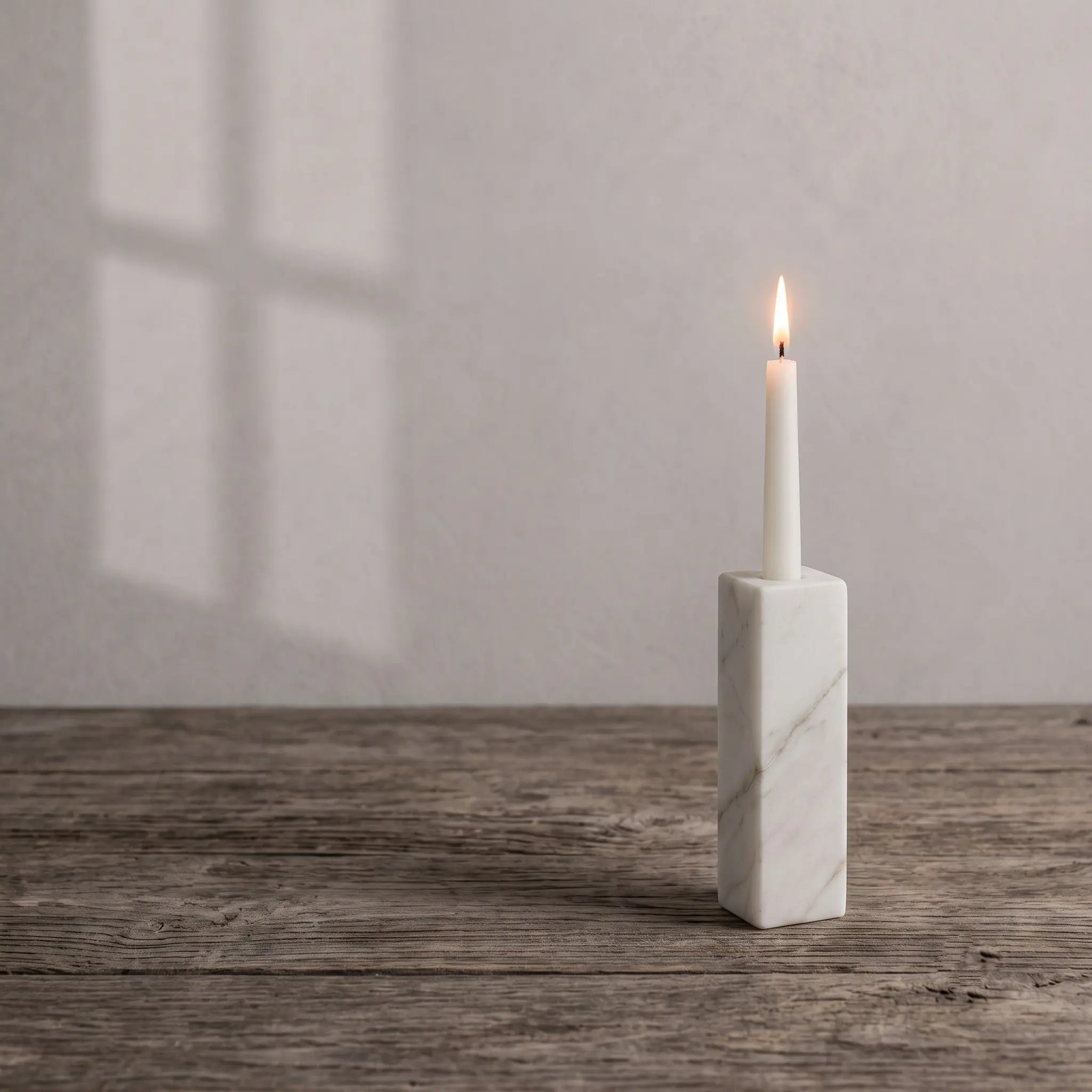 Monolith Candle Holder in White Marble on a wooden desk with window light and a lit taper candle