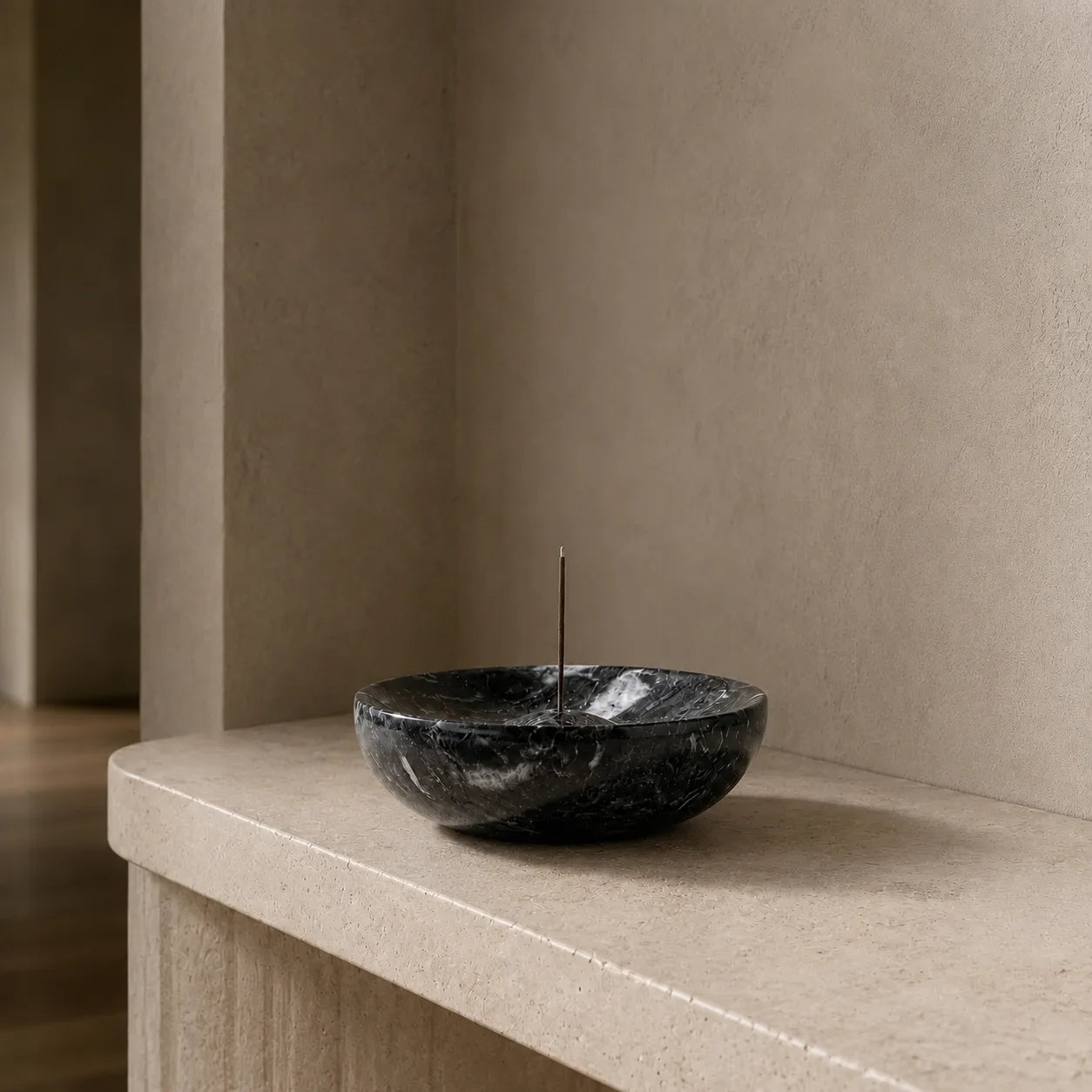 Black marble incense bowl with a slender incense stick on a pale stone entryway console.