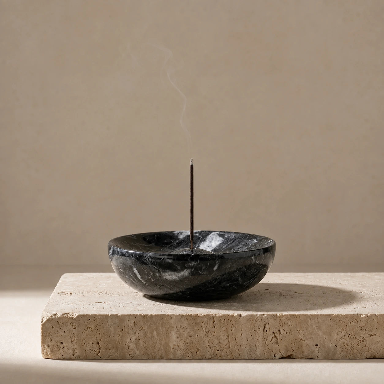 Black marble incense holder bowl with incense stick on a travertine surface