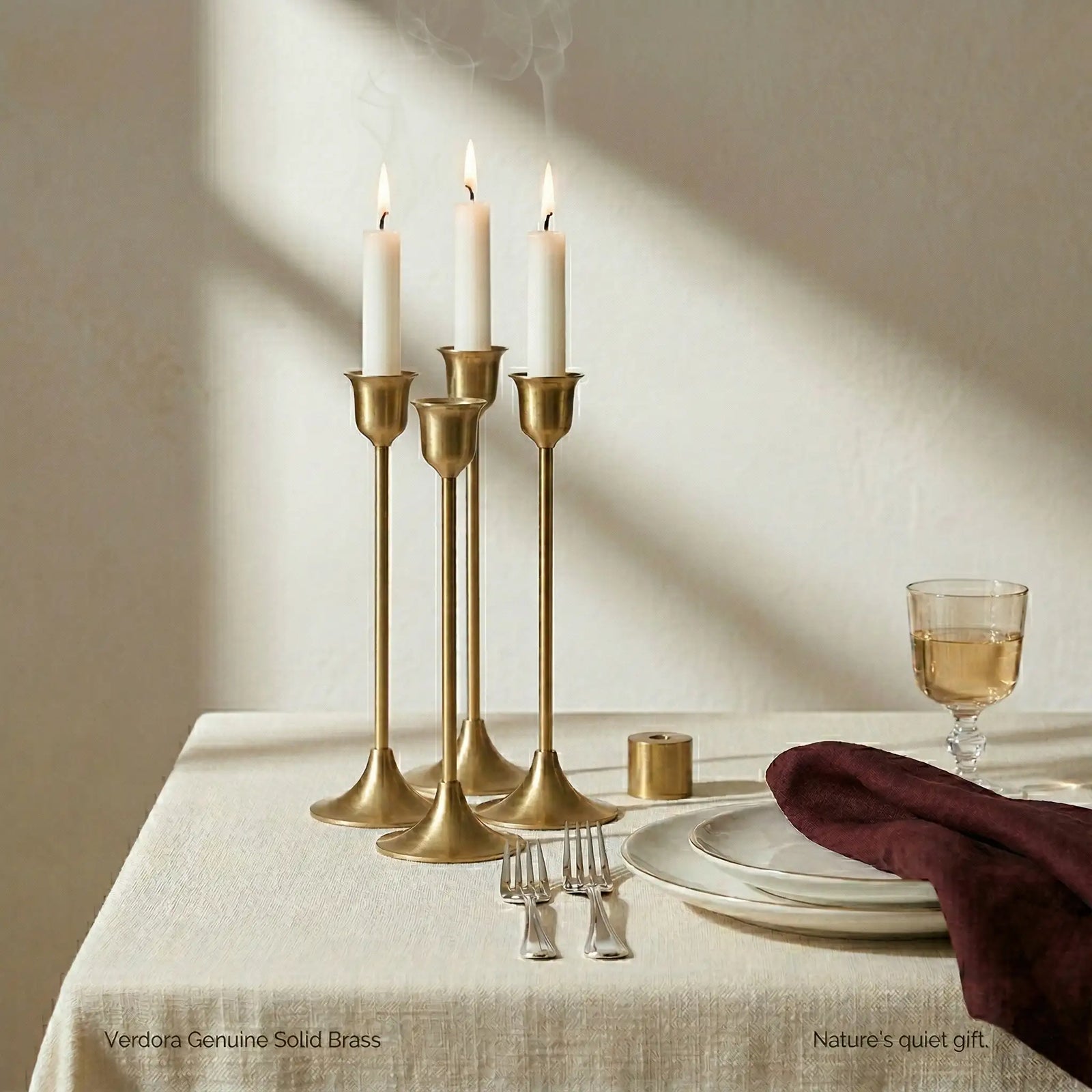 Brass Monolith Trio candlestick holders arranged on a dinner table with wine glasses and elegant tableware.