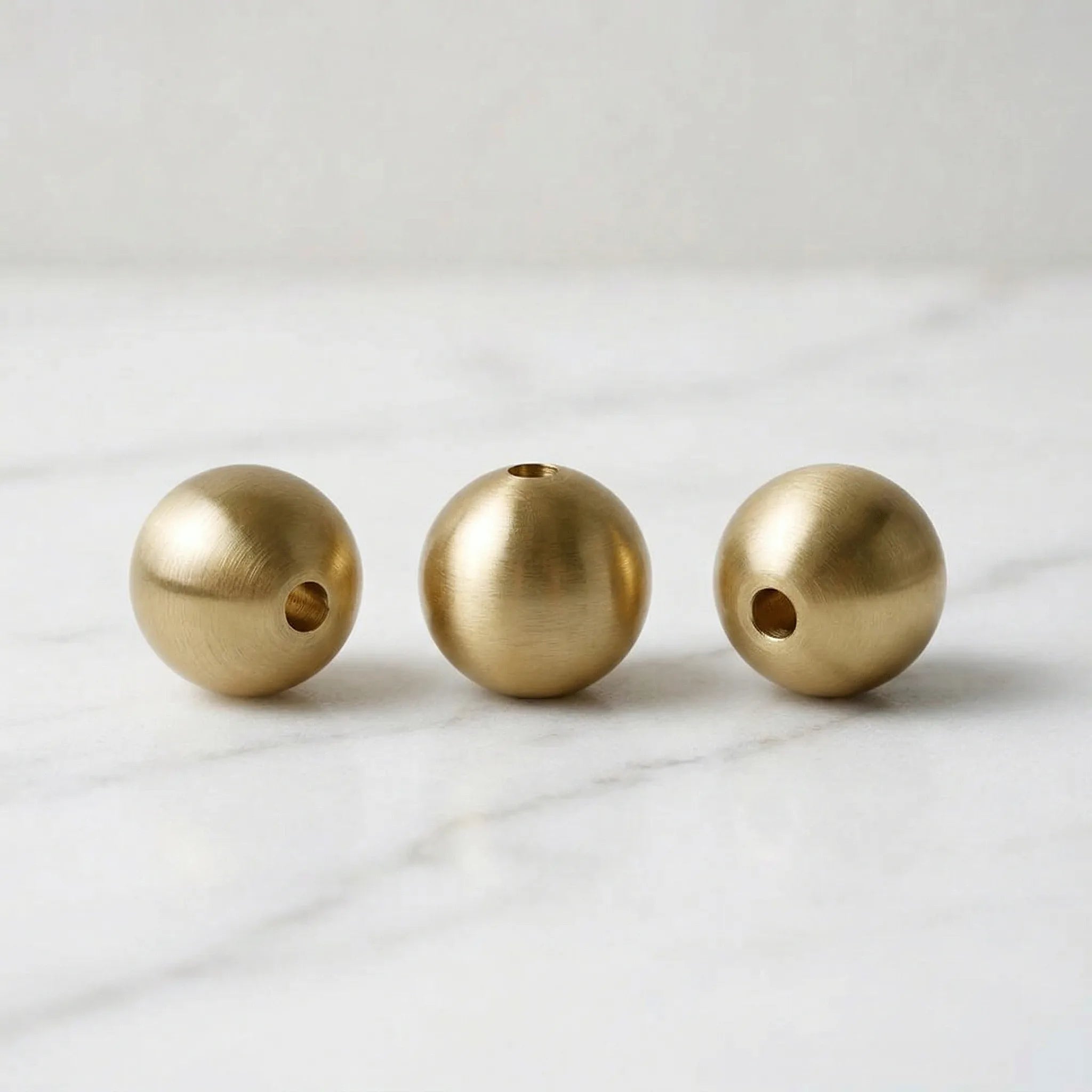 Three handcrafted solid brass sphere incense holders displayed on a white marble surface.