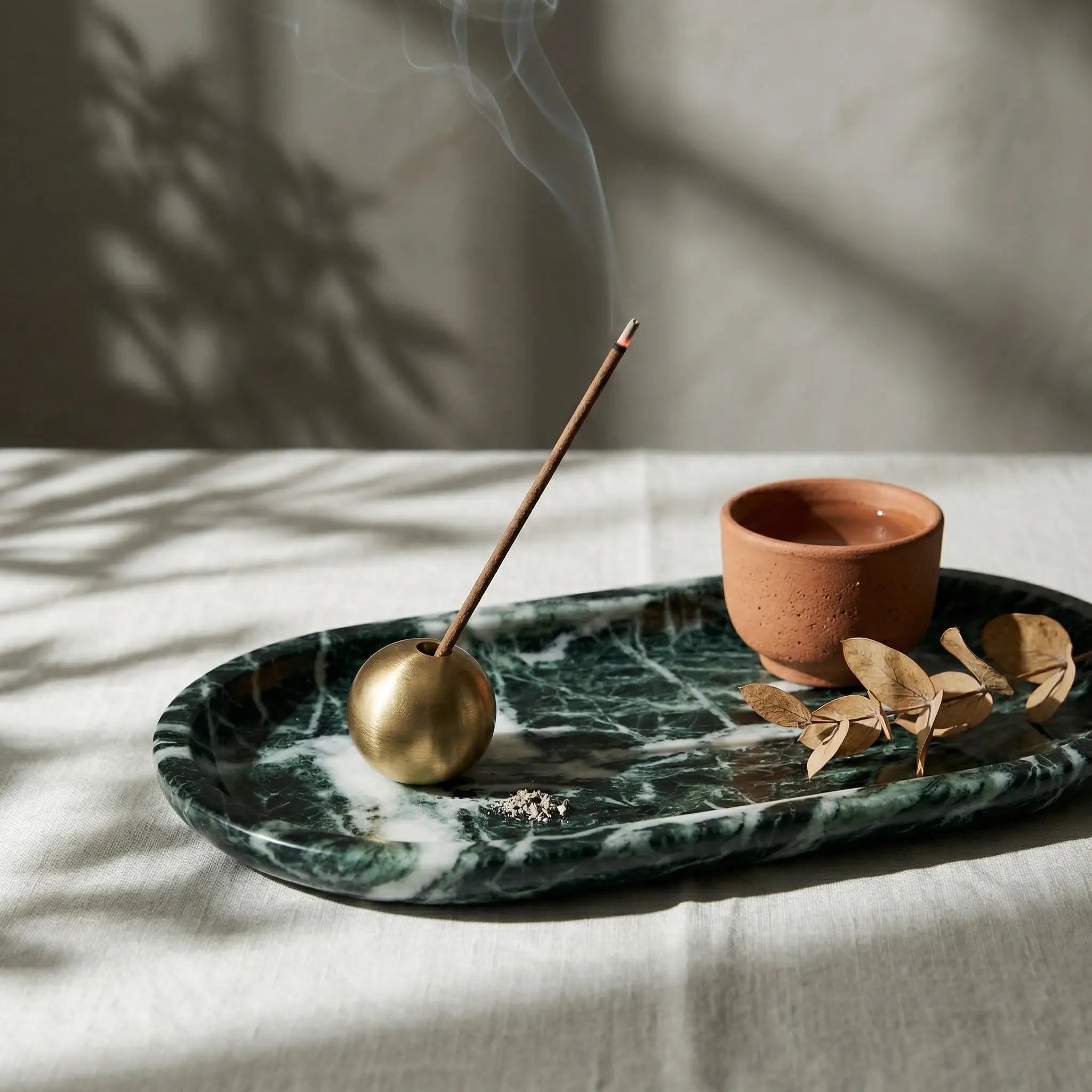 A Brass Sphere Relic holding a burning incense stick on a luxury green marble tray with home decor.