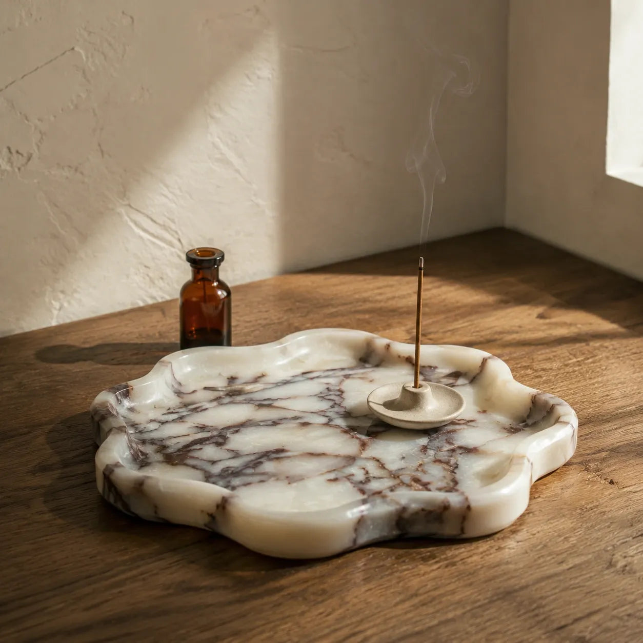 Calacatta Viola marble petal tray styled with an incense holder and amber glass bottle, featuring an organic flower-like silhouette, polished marble edge, and unique grey purple natural veining.