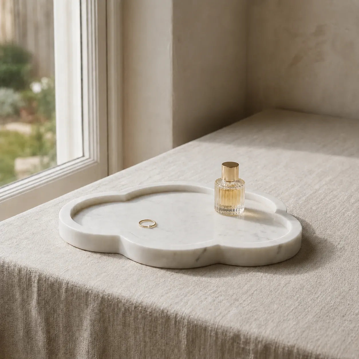 Cloud-shaped white marble tray on a linen bedside surface with a perfume bottle and gold ring, highlighting its organic silhouette, rounded edges, and polished natural stone finish.