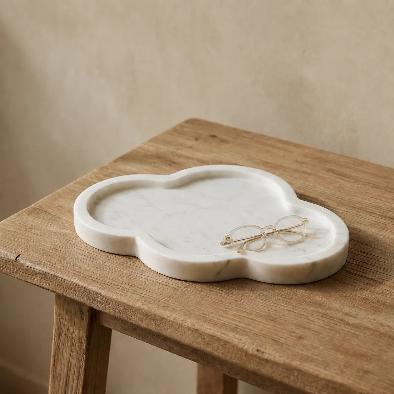 Cloud-shaped white marble tray on a light oak desk with reading glasses, highlighting its organic silhouette, rounded edges, and polished natural marble finish.