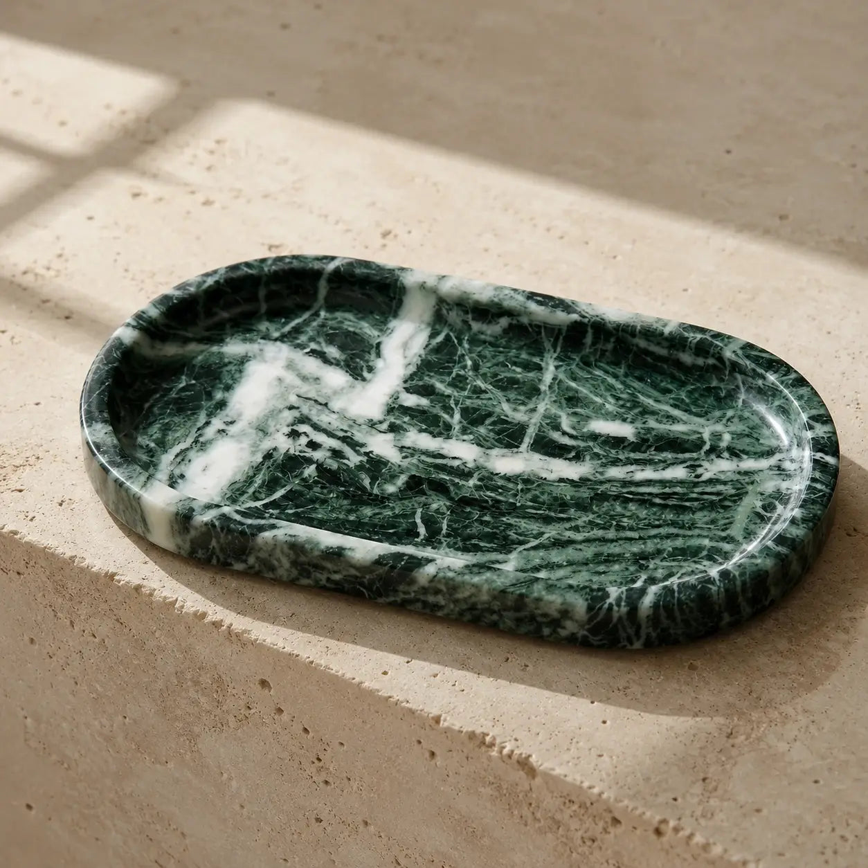 Deep green natural marble tray with white mineral veining on a limestone surface, showcasing its rounded rectangular shape, shallow carved design, polished edge, and unique stone variation.