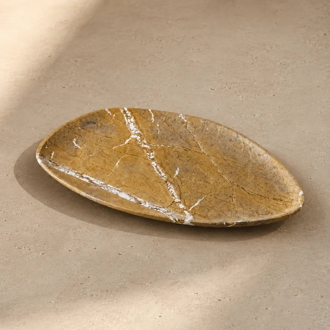 Golden yellow marble leaf-shaped tray on a limestone surface, showcasing its organic silhouette, polished stone edge, and unique natural mineral veining.