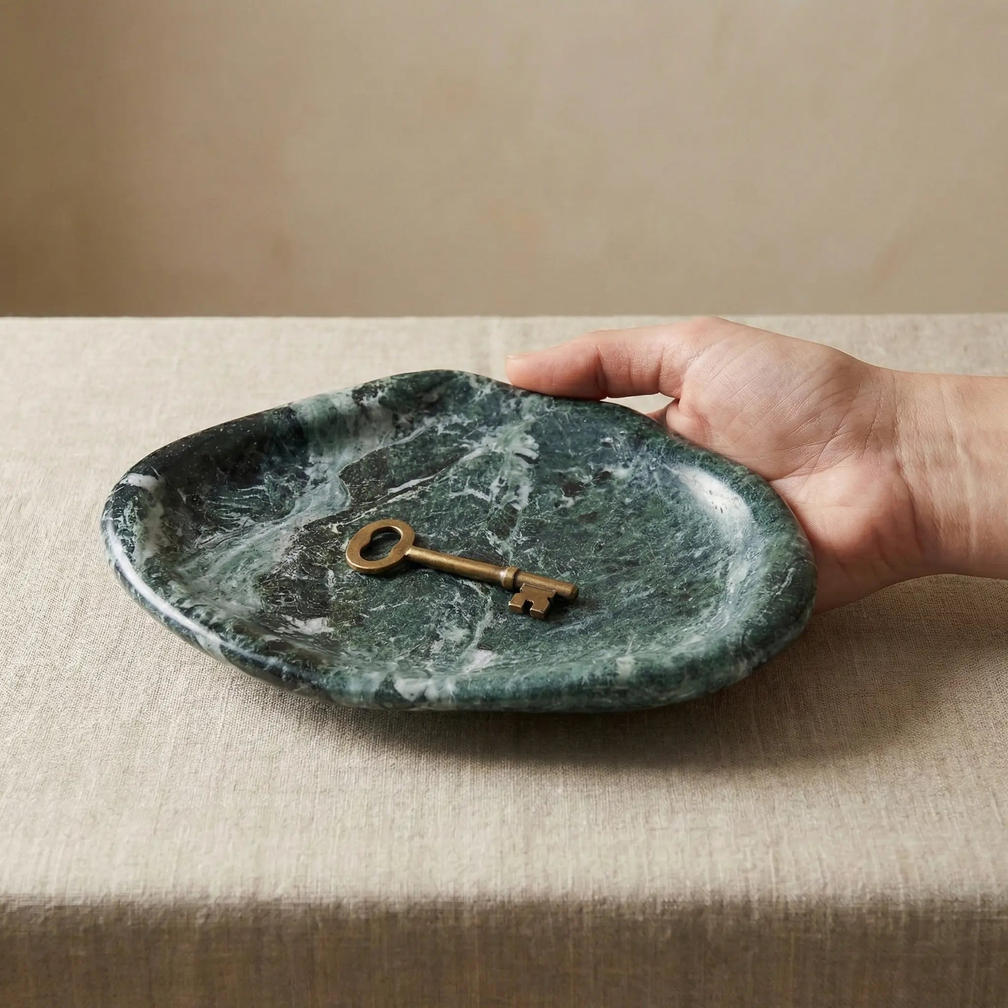 Hand holding a key over Marble Cloud Tray in forest green stone to show scale and size reference