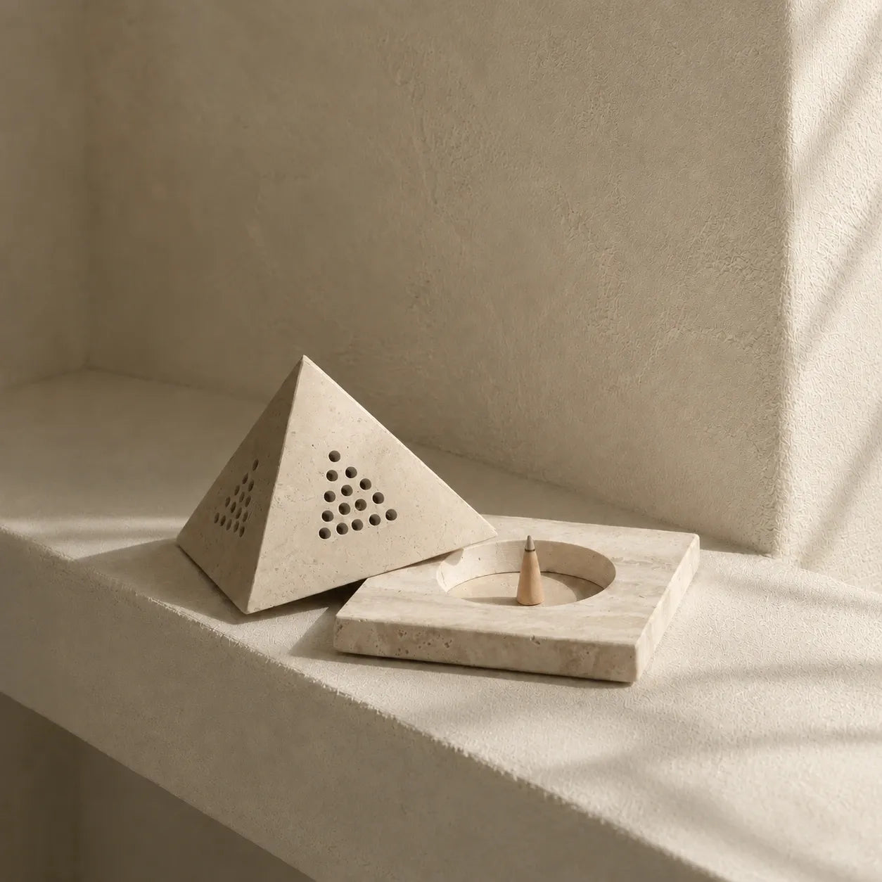 Natural travertine incense holder styled on an architectural plaster shelf with a geometric stone cover and minimalist interior setting
