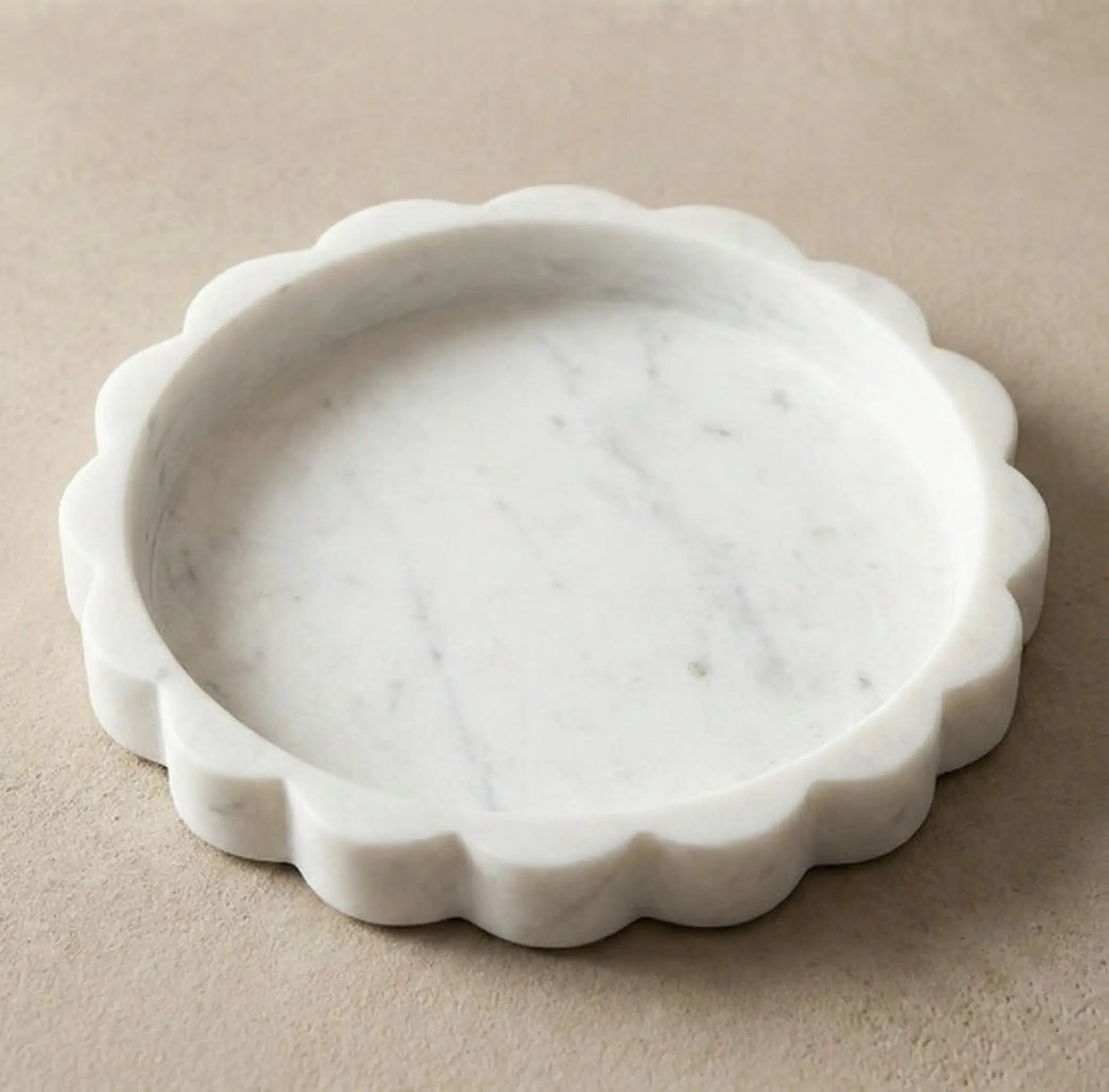 Top view of a handcrafted scalloped circular white marble tray with natural grey veining and sawtooth edges.
