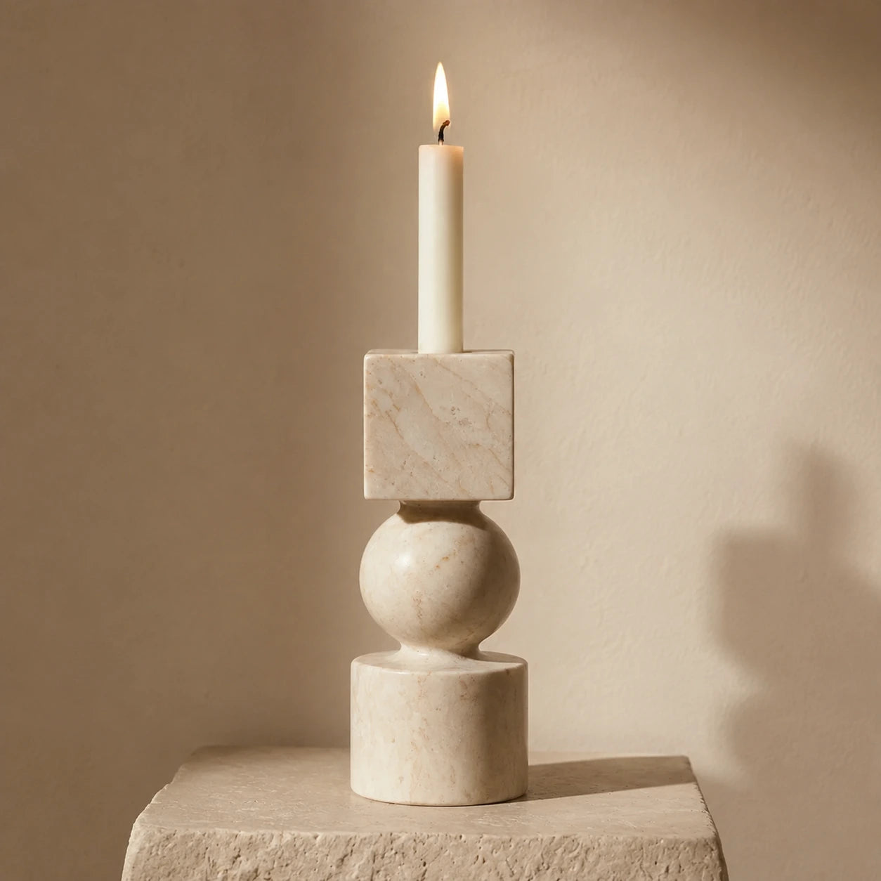 Sculptural natural stone candle holder with a taper candle, displayed on a travertine surface with soft afternoon light.