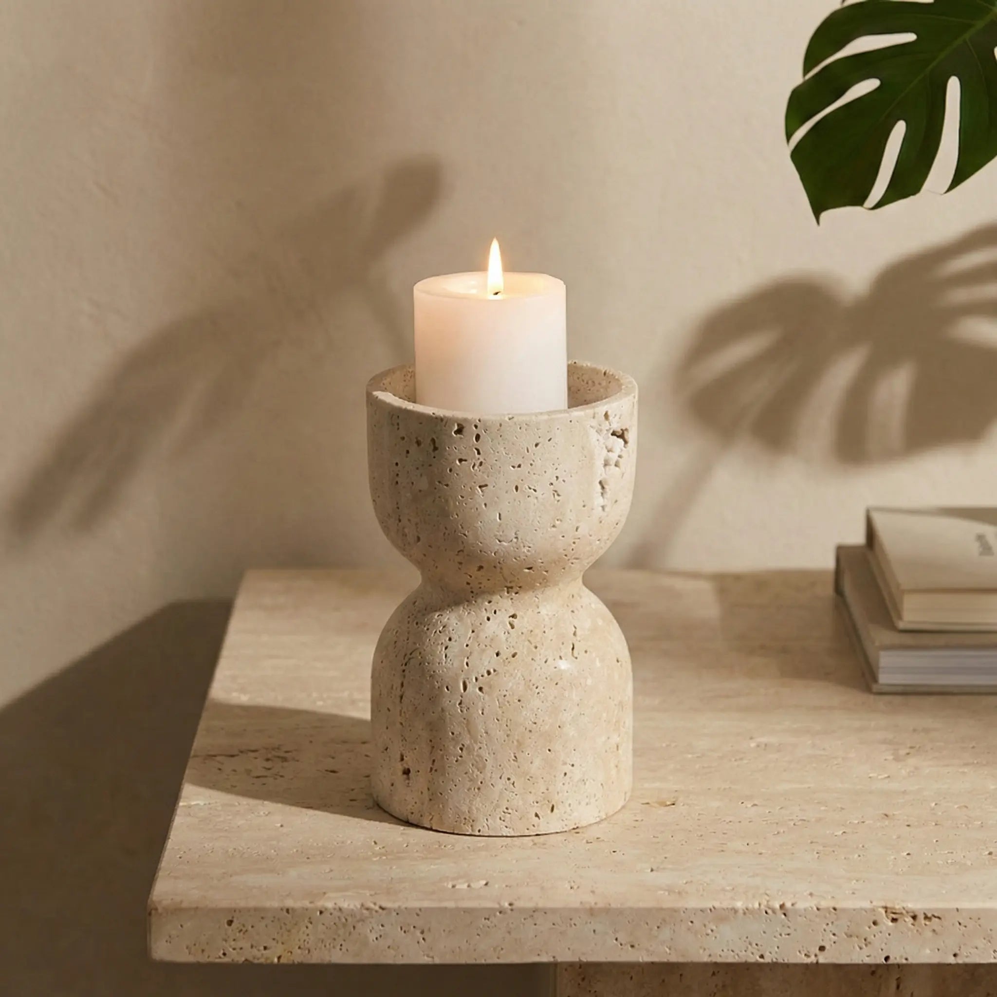 Travertine Hourglass Holder with a burning candle on a wooden console under warm ambient lighting.