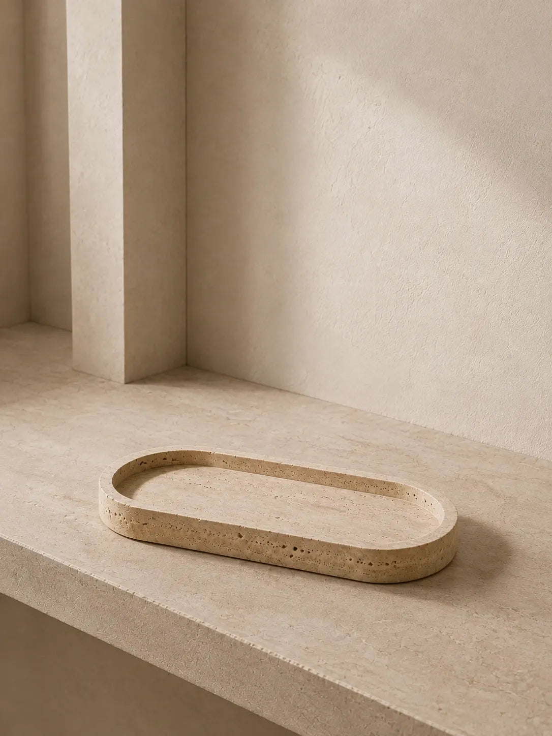 Natural travertine long tray with a flat surface and low raised rim in a quiet architectural interior, illuminated by soft morning light highlighting the stone texture and natural pores.