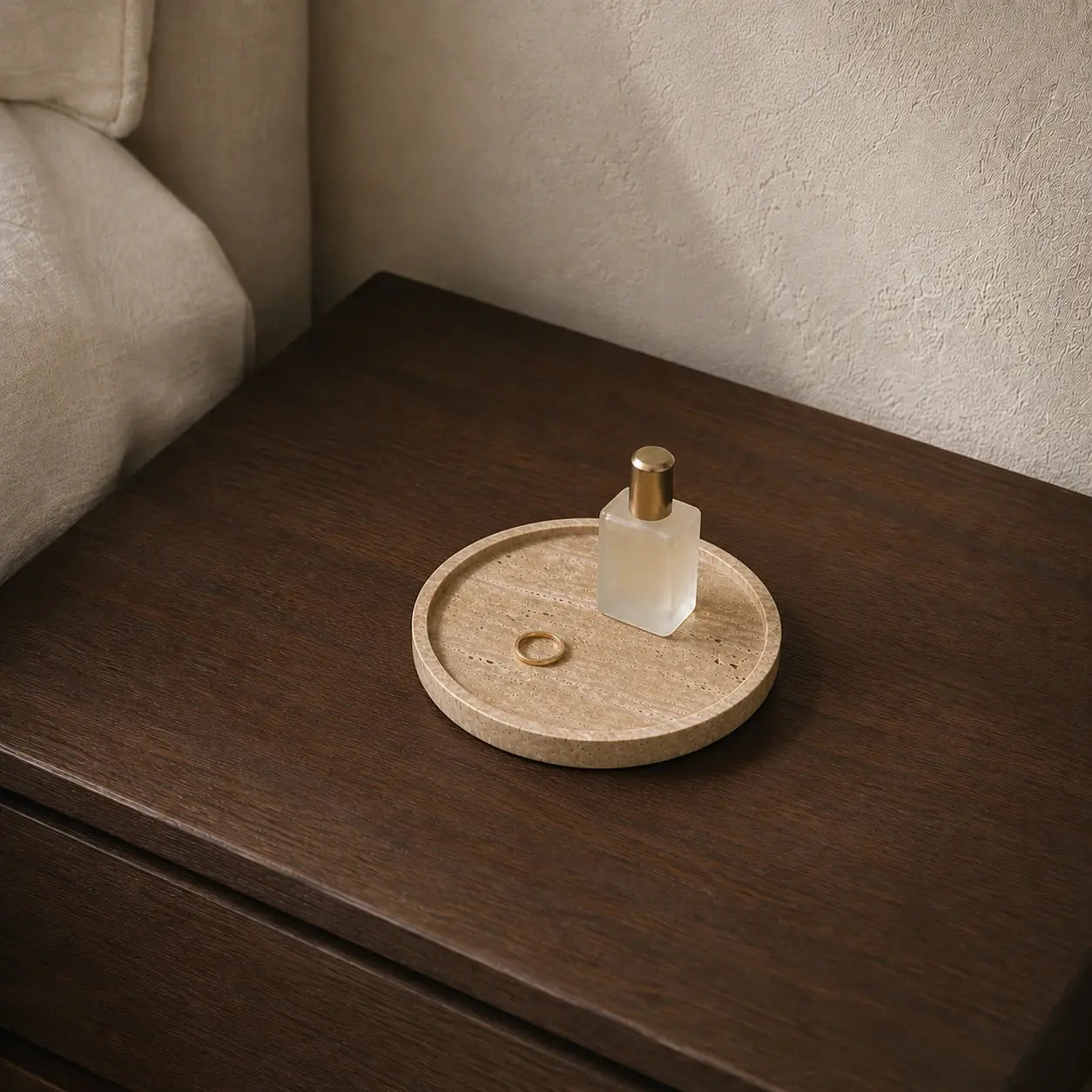 Small 20 cm round travertine tray styled with a perfume bottle and ring on a dark wood bedside table