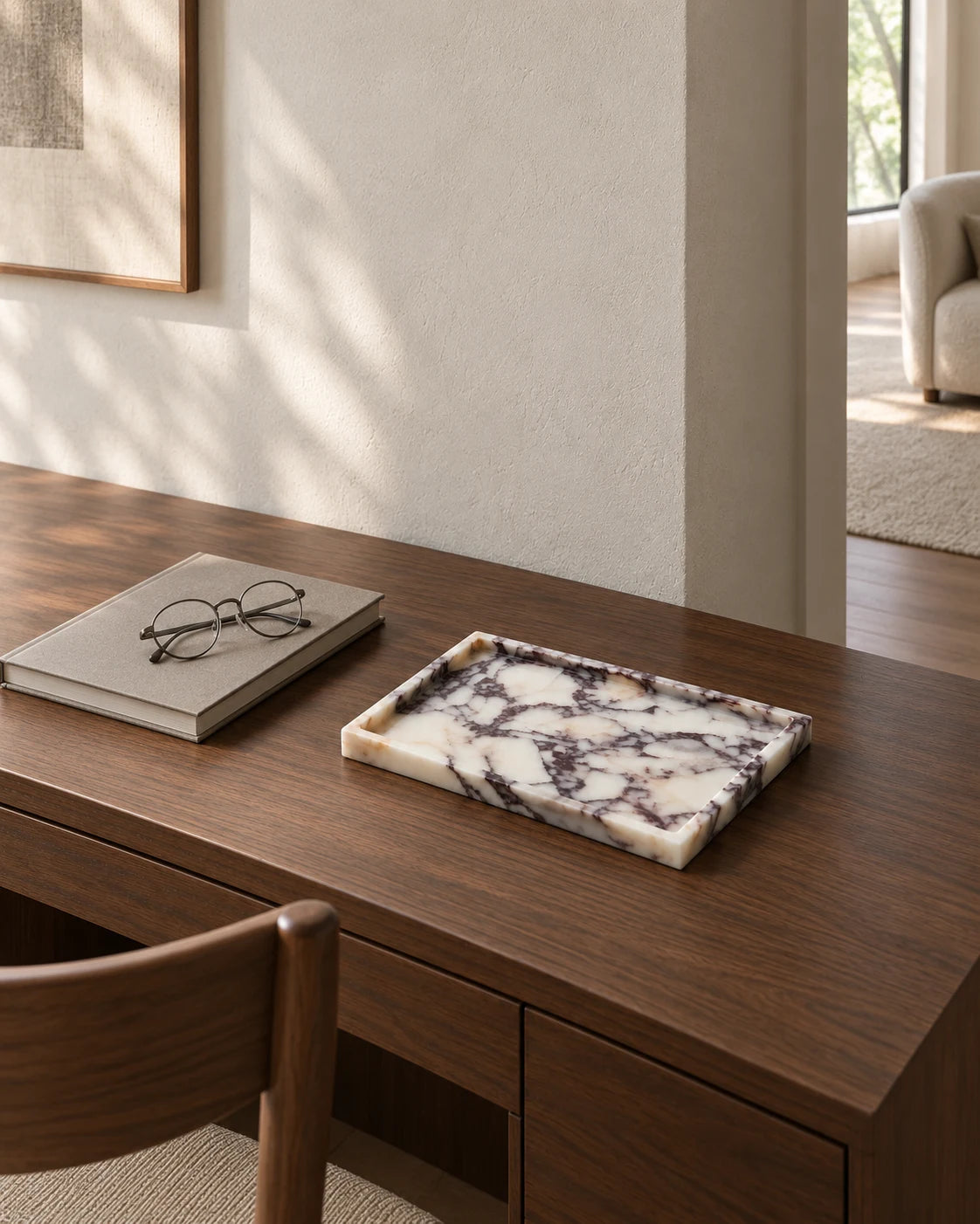 Rectangular Calacatta marble tray on a walnut reading desk beside a book and glasses, with a wooden chair in the foreground and a sunlit living room beyond.